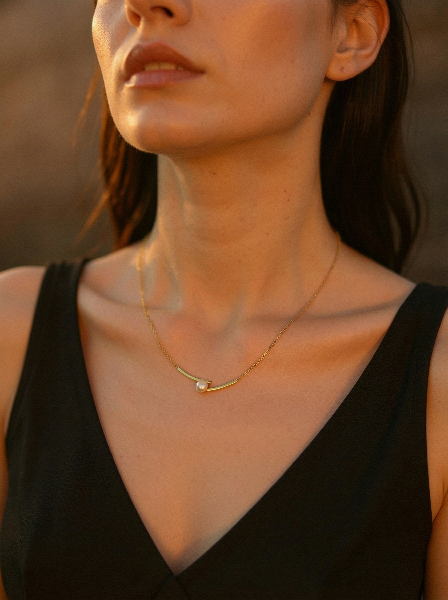 Woman wearing a delicate gold necklace with a small pendant against a blurred background