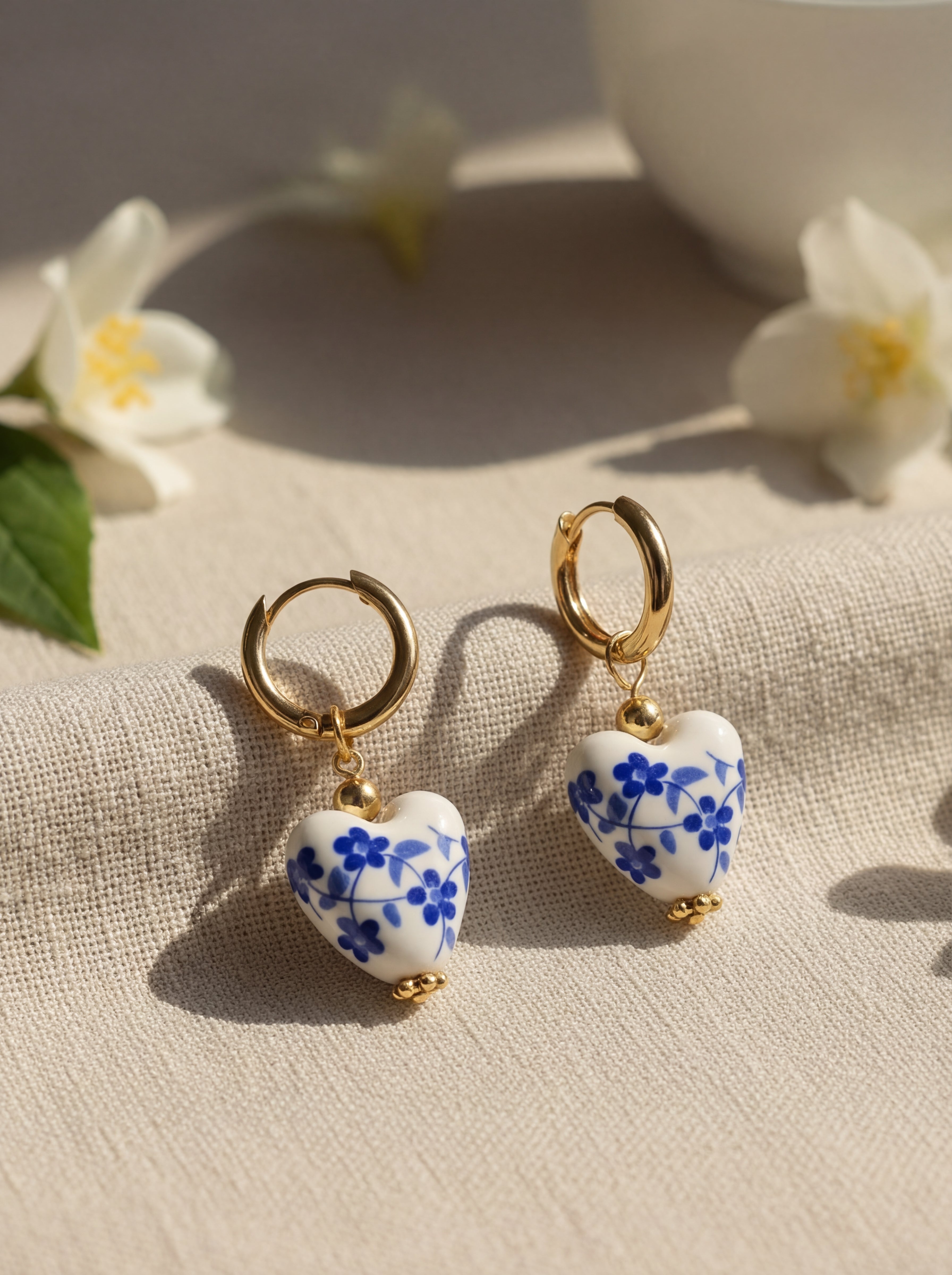 Heart-shaped earrings with blue floral design on a beige fabric background with flowers.