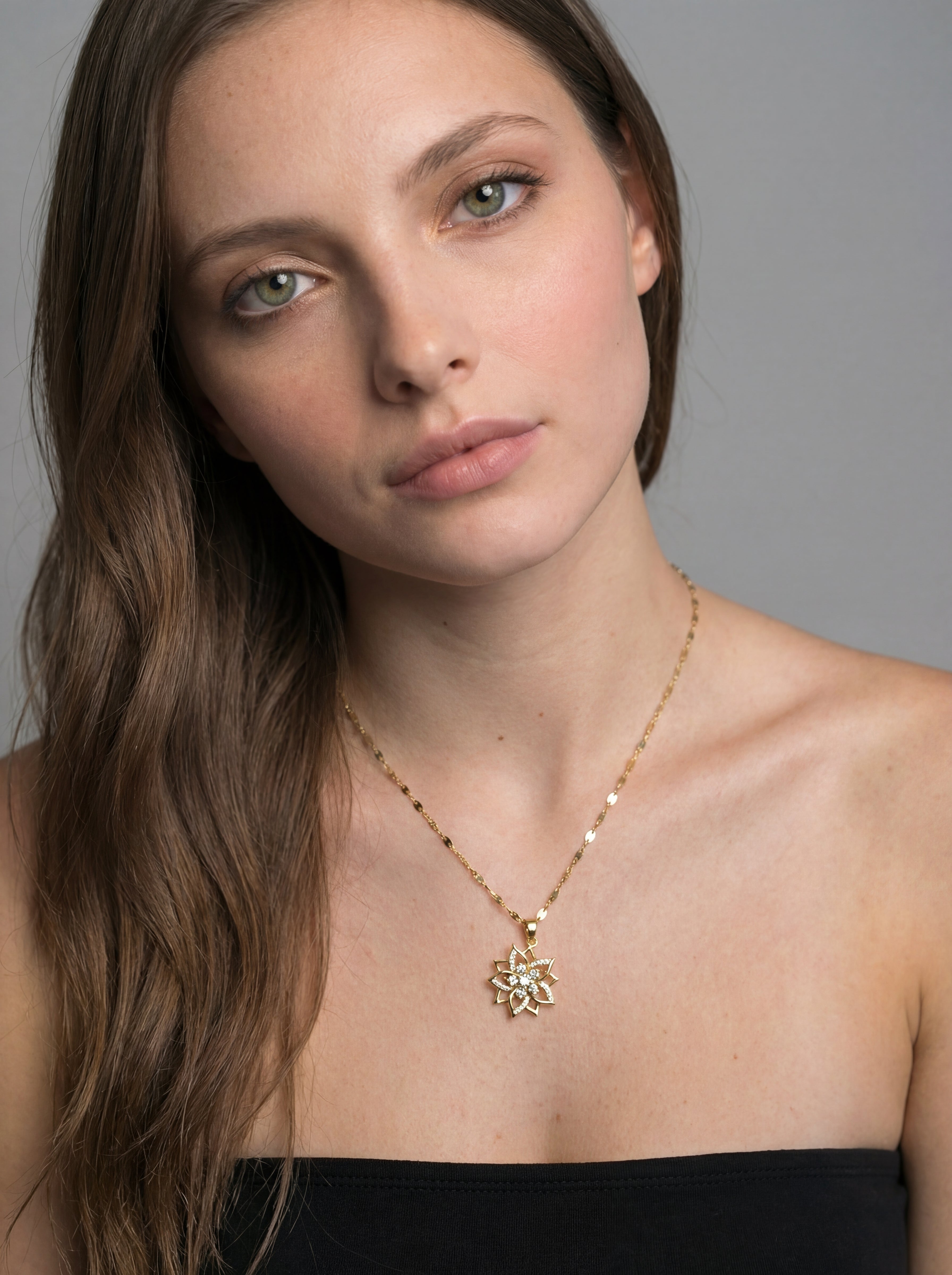 Woman wearing a gold necklace with a pendant against a gray background