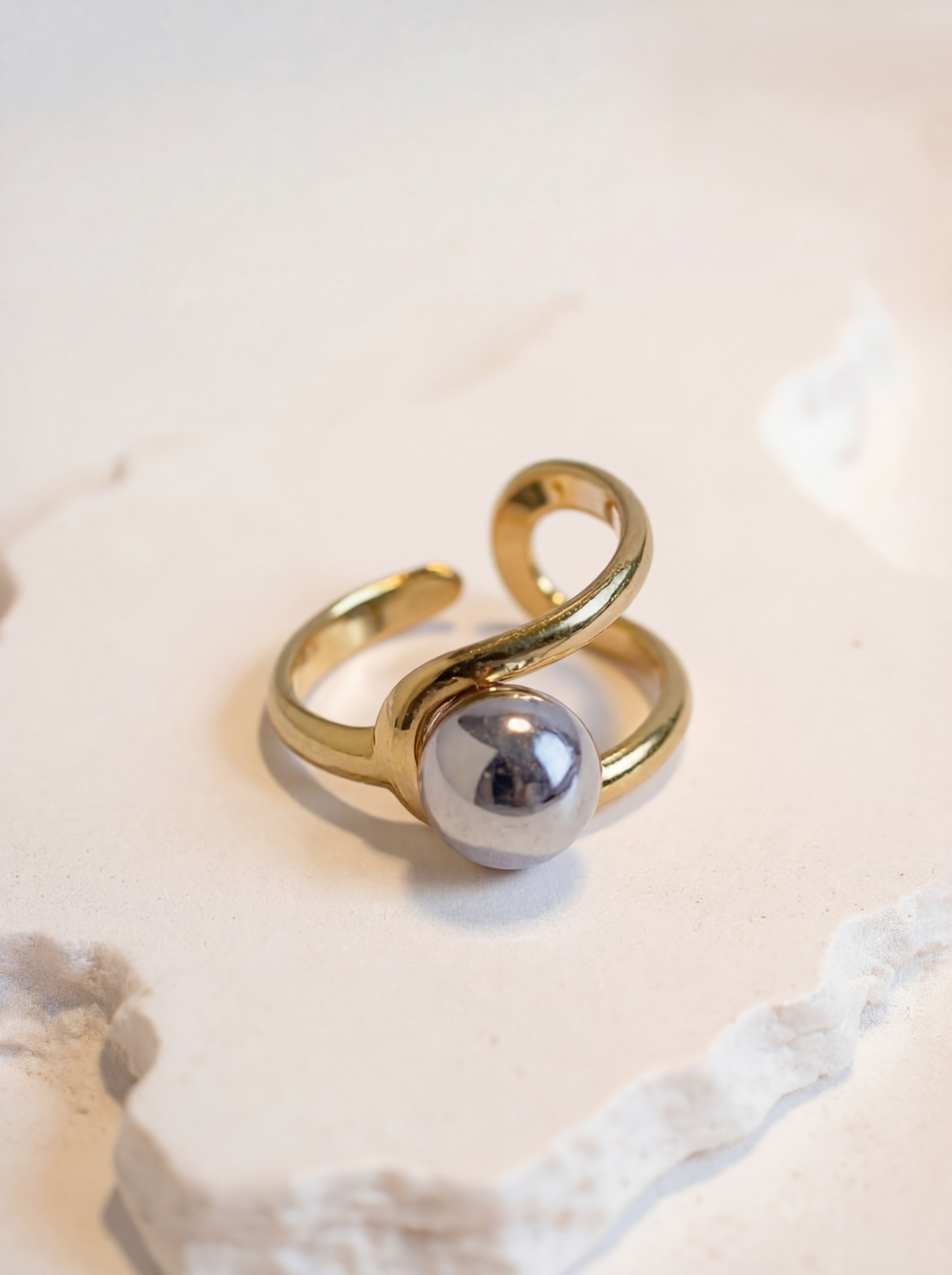 Gold ring with a silver sphere on a light background