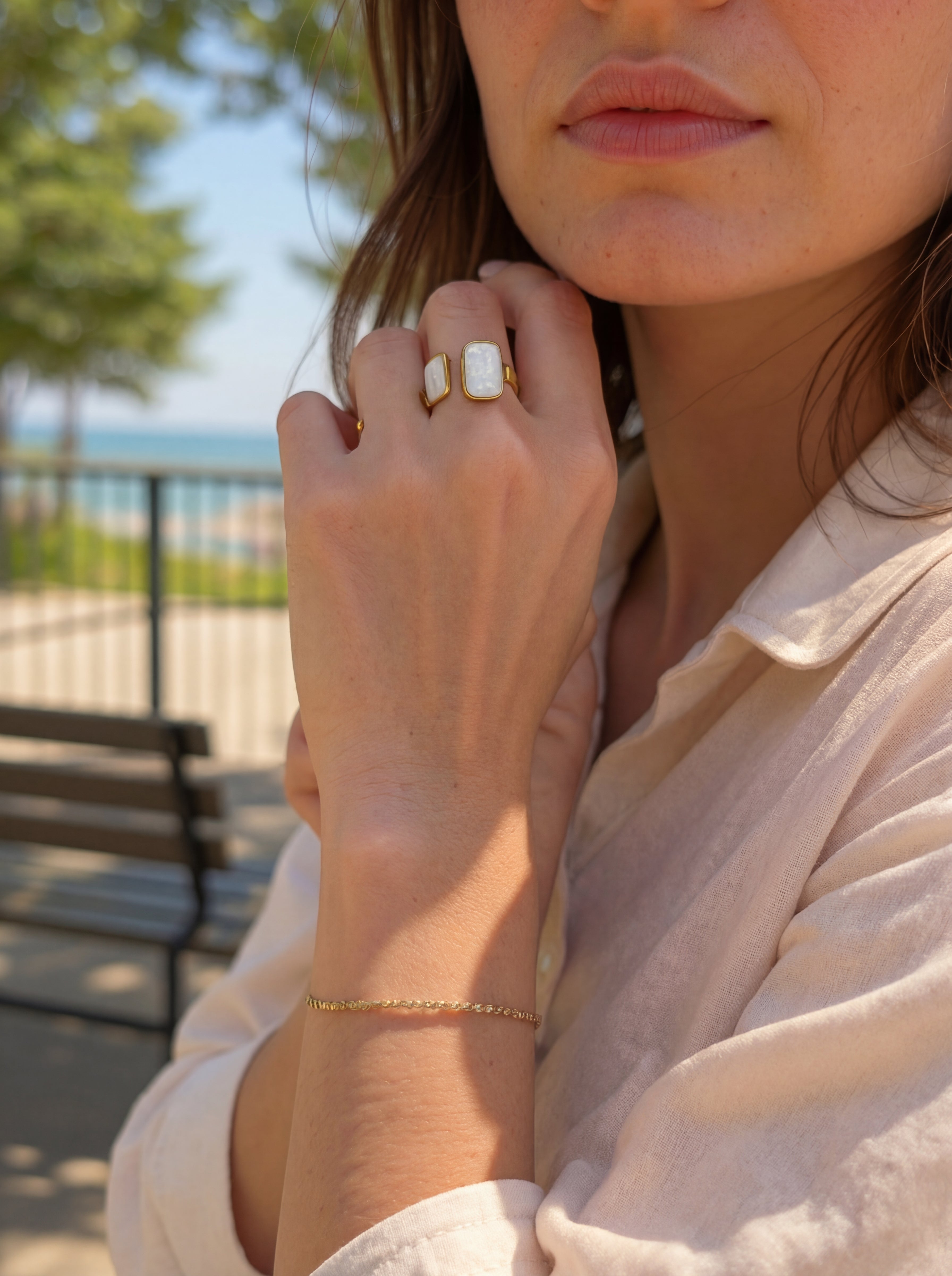 Close-up of a person wearing a gold ring and bracelet with a blurred outdoor background