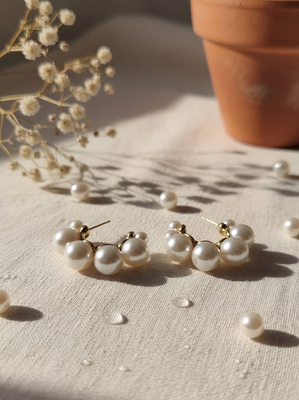 Pearl earrings on a textured surface with a potted plant in the background
