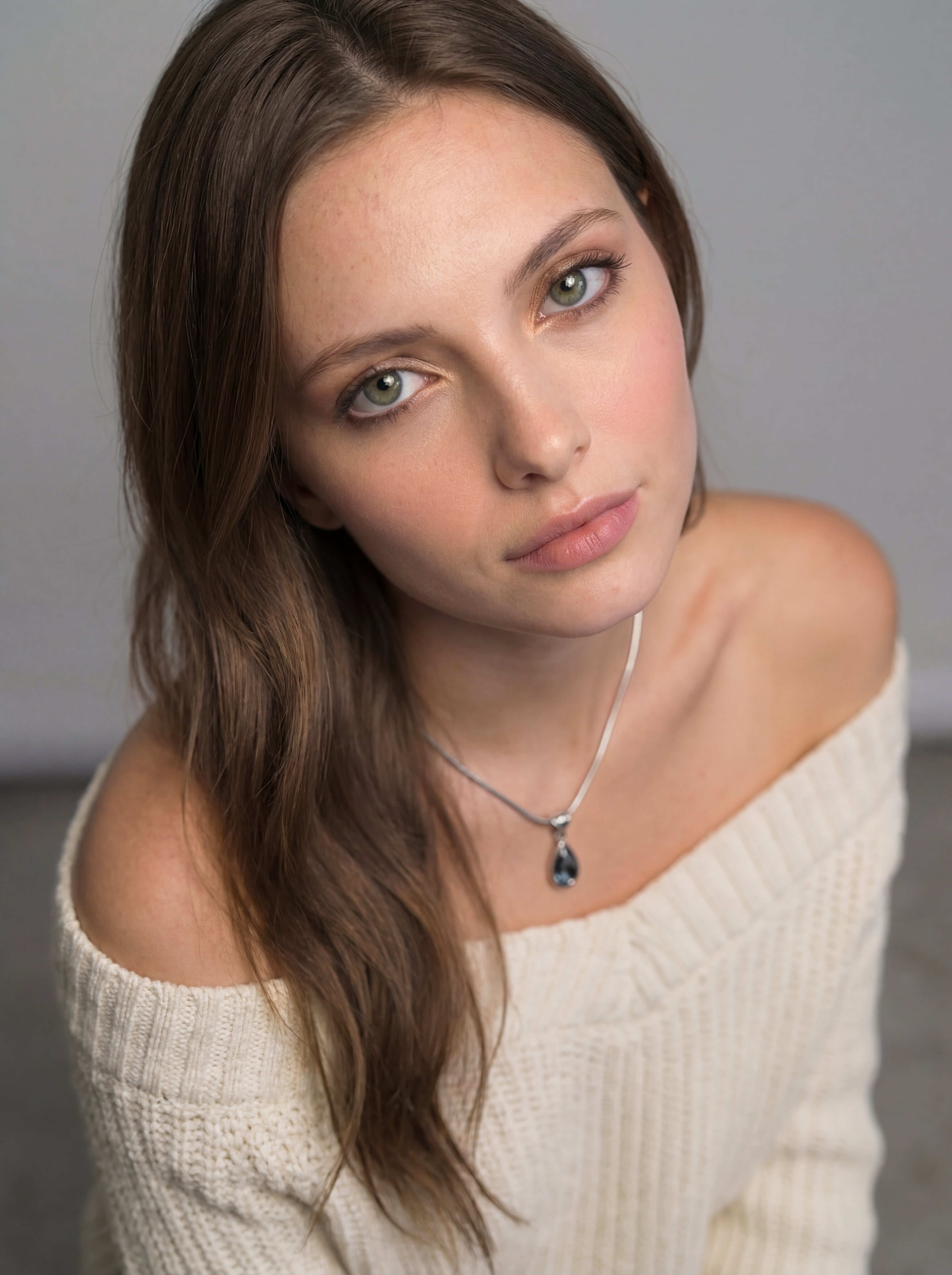 Woman wearing a white off-shoulder sweater with a gray background