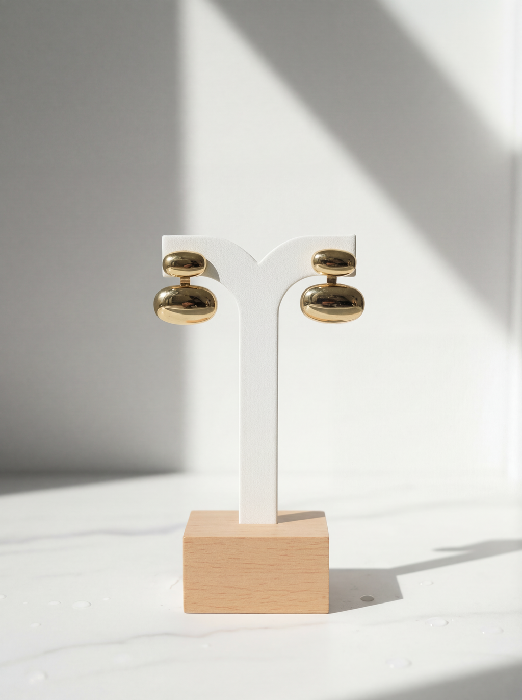 Gold earrings on a wooden stand against a white background