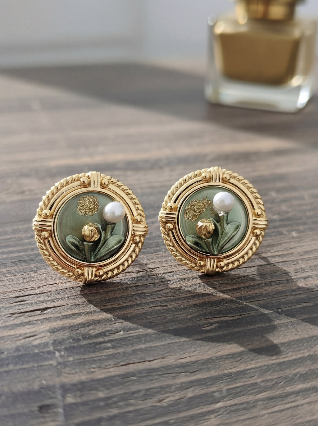Pair of gold earrings with green floral design on a wooden surface