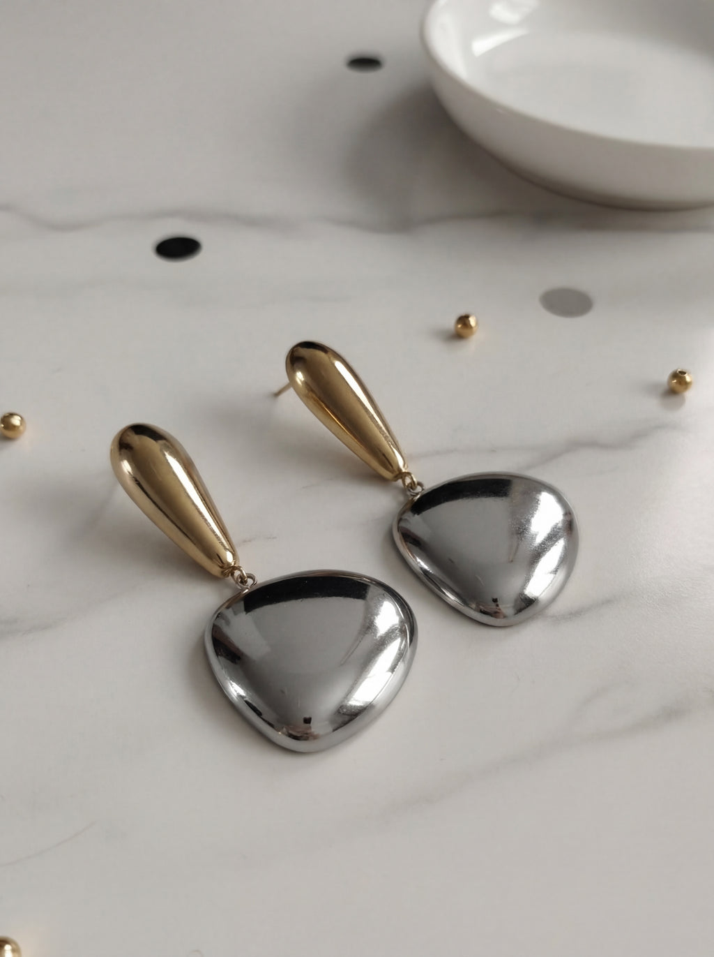 Pair of gold and silver heart-shaped earrings on a light surface.