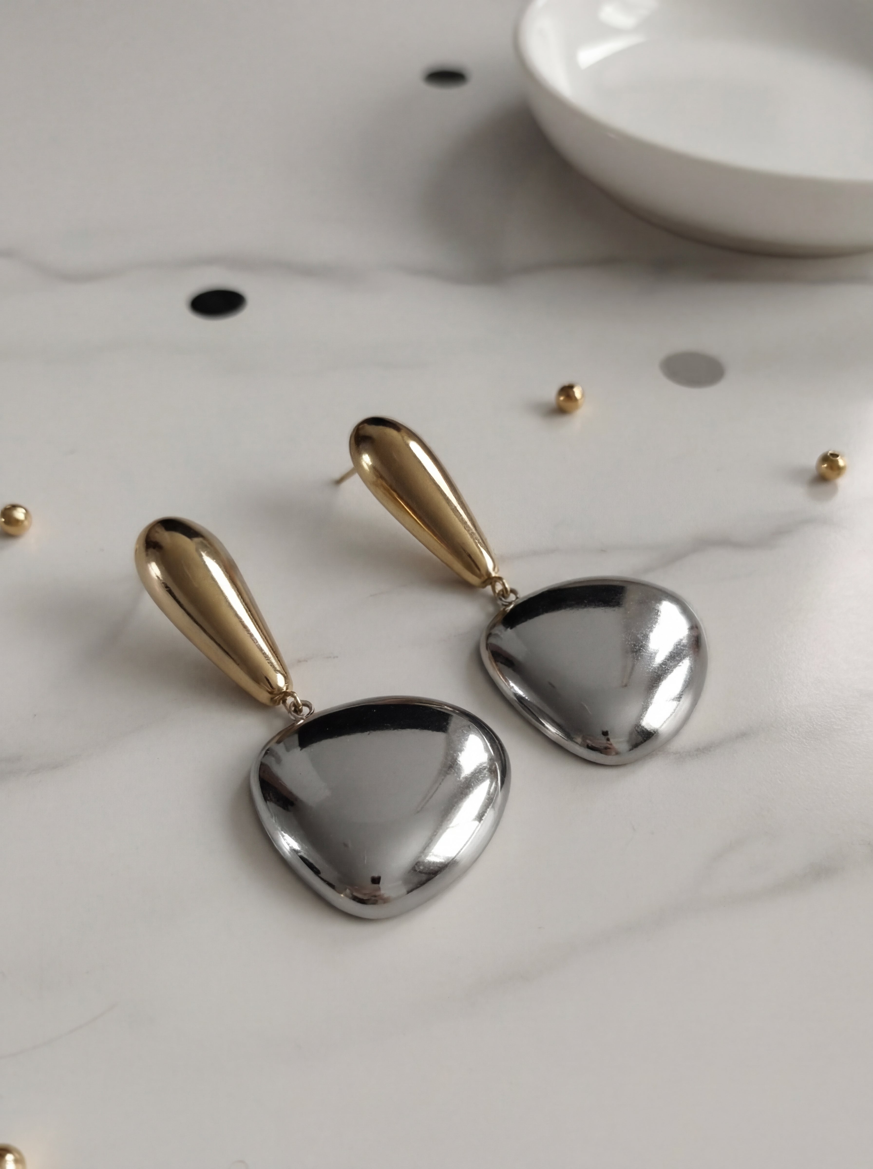 Pair of gold and silver heart-shaped earrings on a light surface.