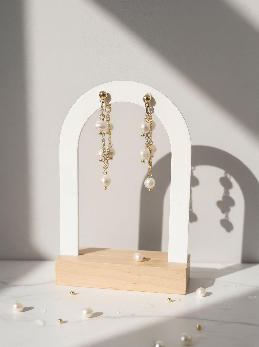 Pearl earrings on a white arch stand with a soft shadow on a light background