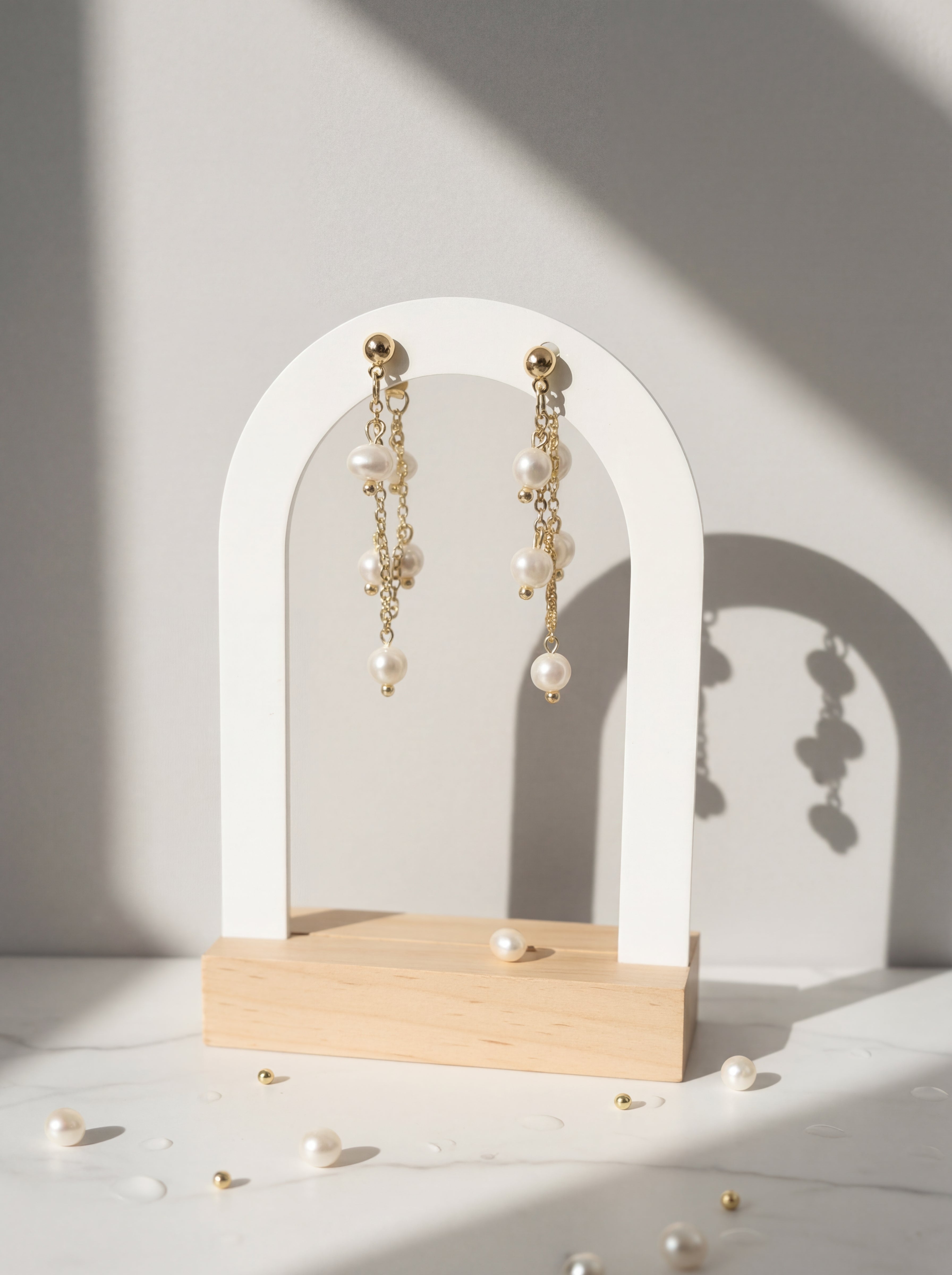 Pearl earrings on a white arch stand with a soft shadow on a light background