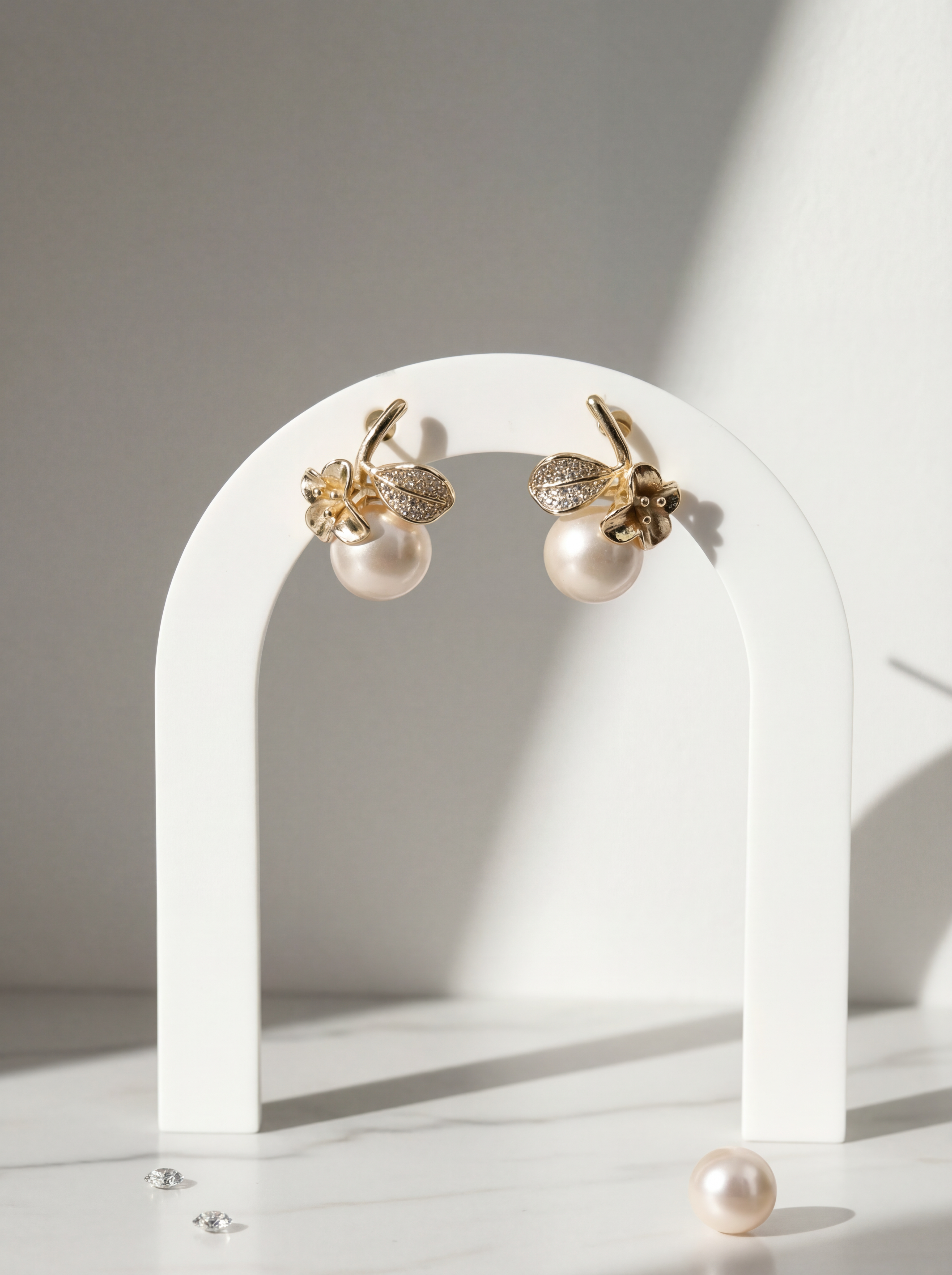 Gold earrings with pearl-like beads on a white arch stand.