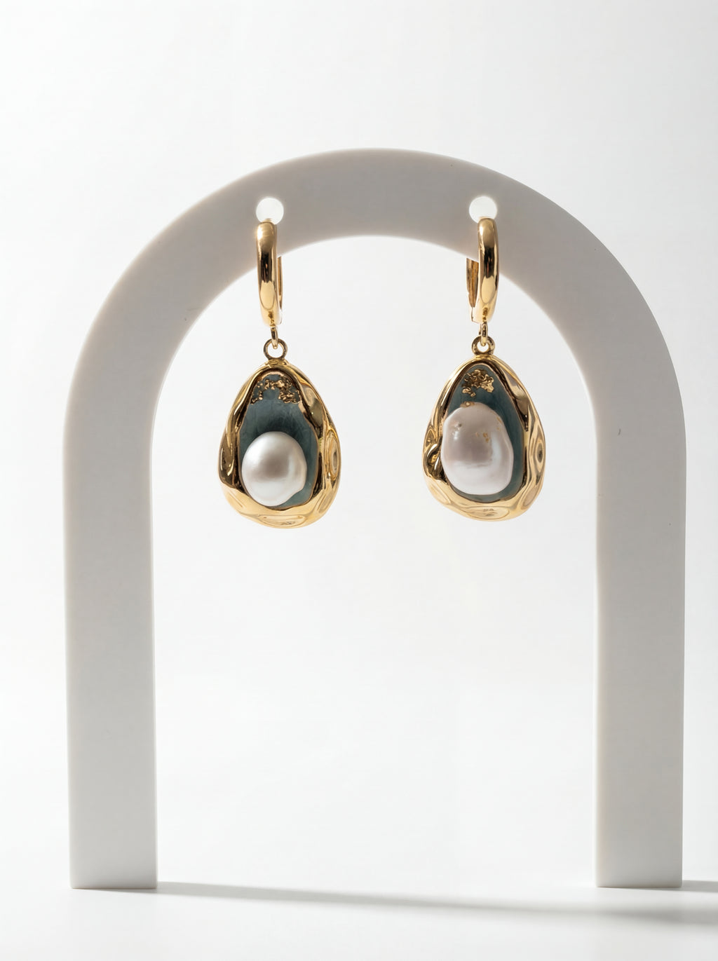 Gold earrings with pearl-like stones on a white arch stand