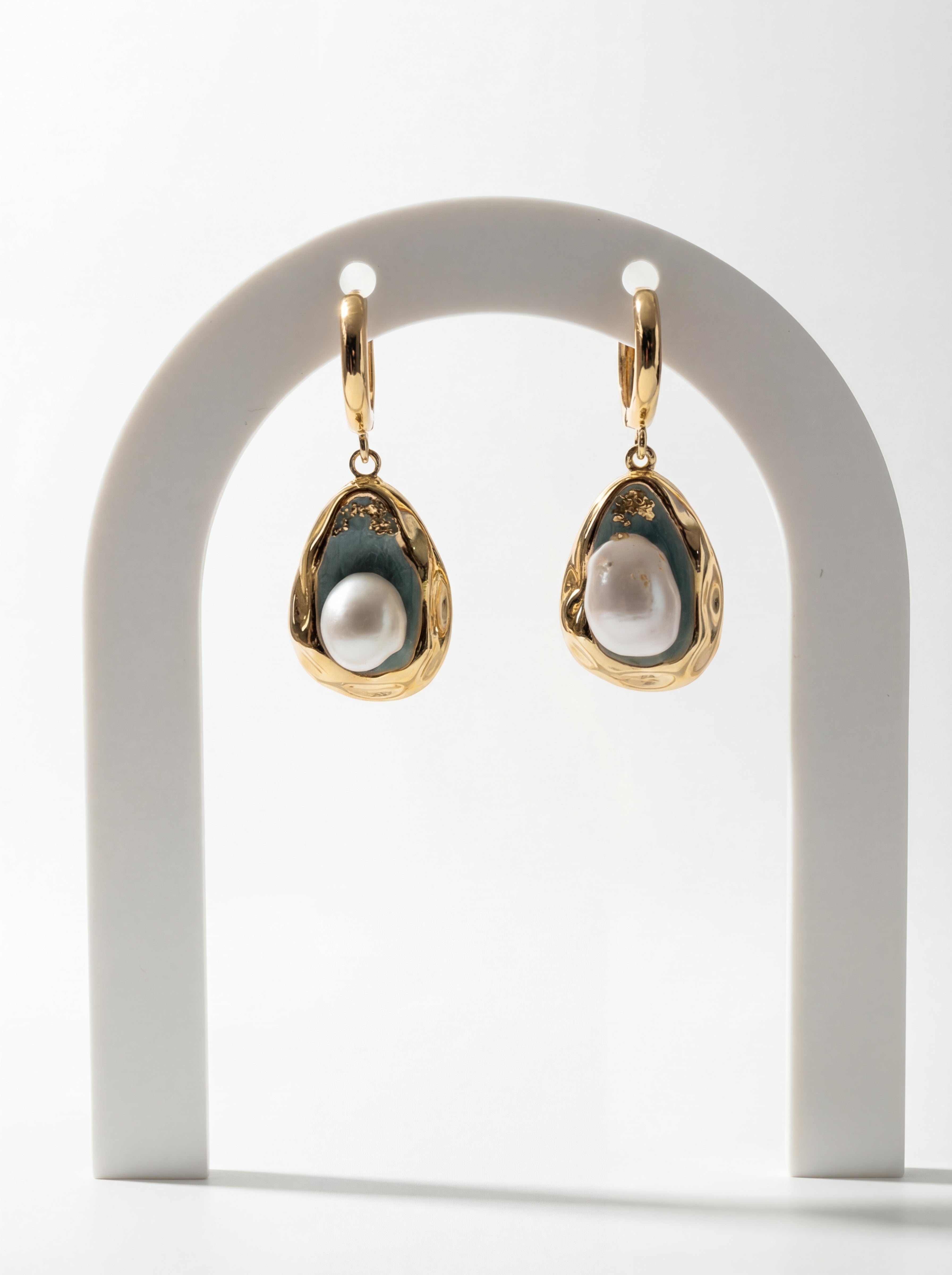 Gold earrings with pearl-like stones on a white arch stand
