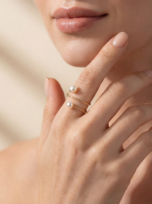 Close-up of a hand wearing a gold ring with pearls on a neutral background