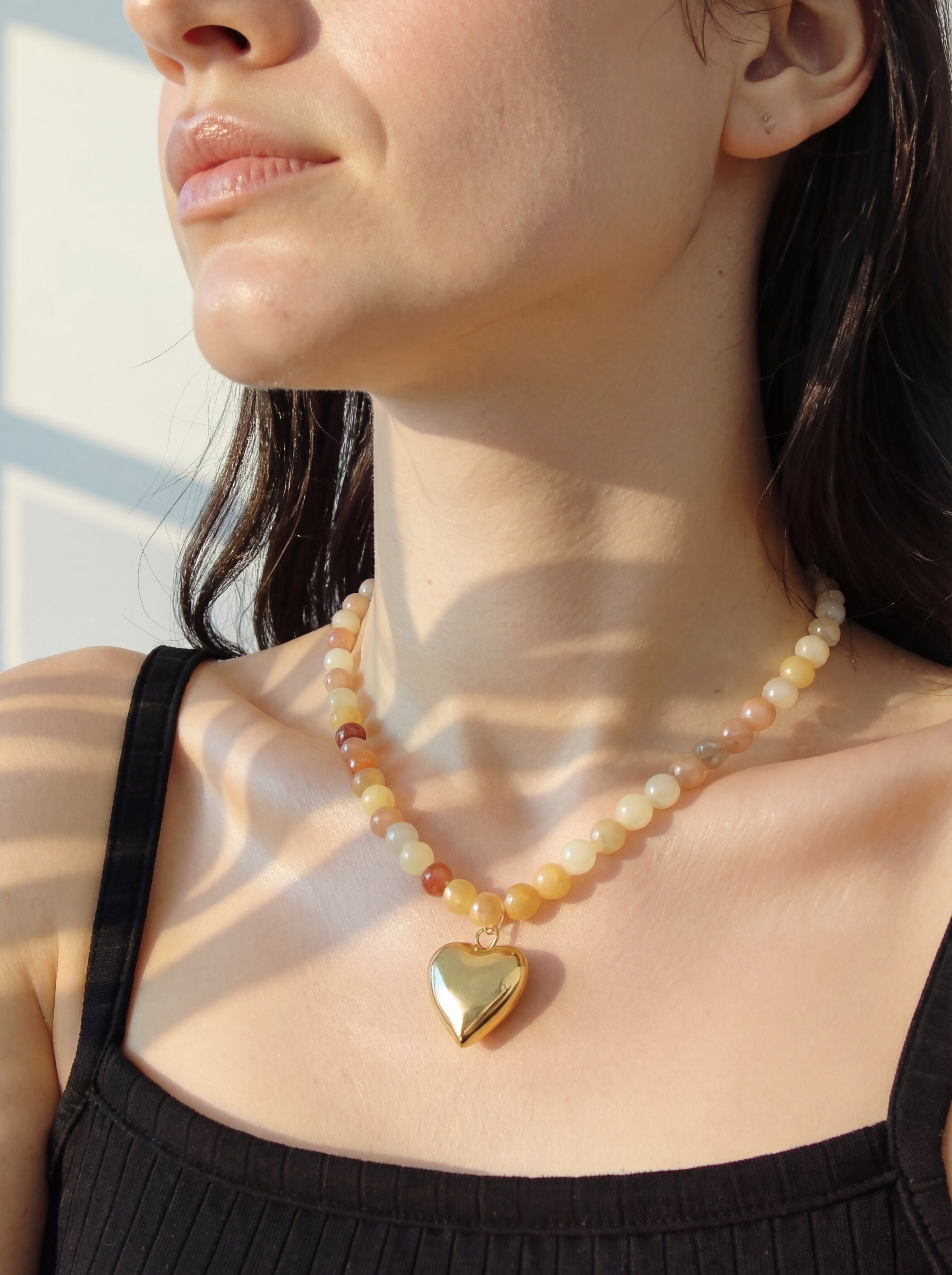Close-up of a woman wearing a necklace with a heart pendant, sunlight casting shadows.