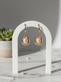 Gold earrings with pink gemstones on a white stand with a gray background