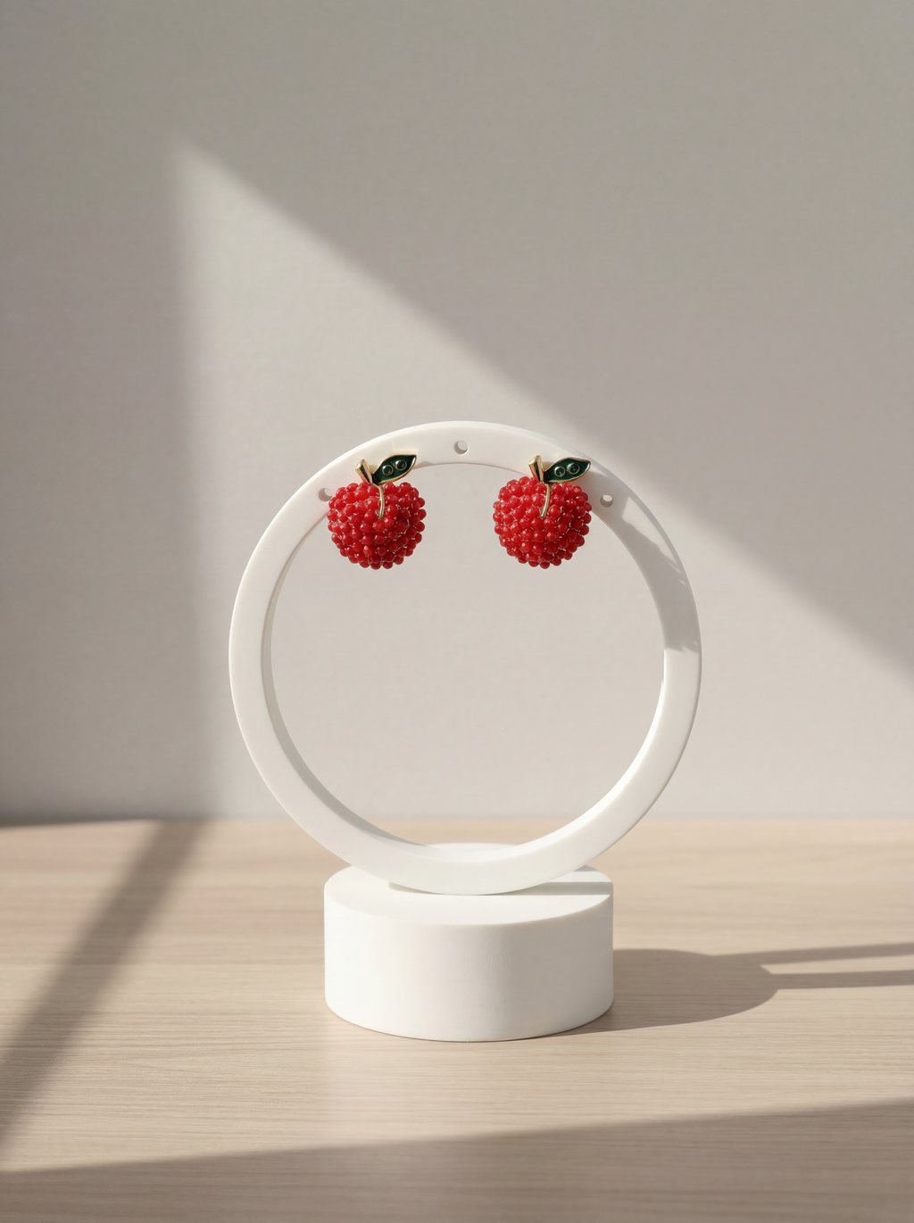 Pair of red berry earrings on a white circular stand against a neutral background