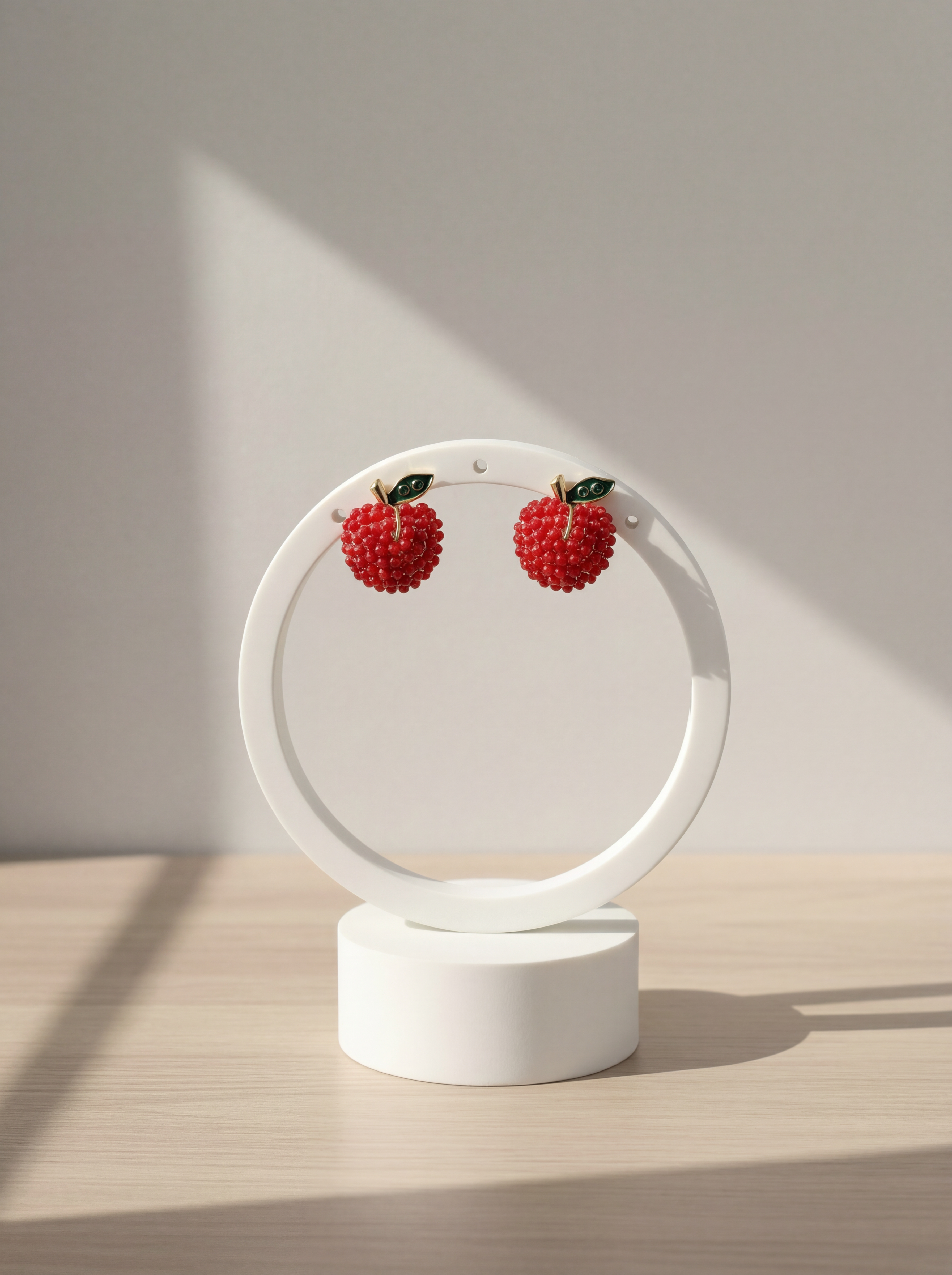 Pair of red berry earrings on a white circular stand against a neutral background