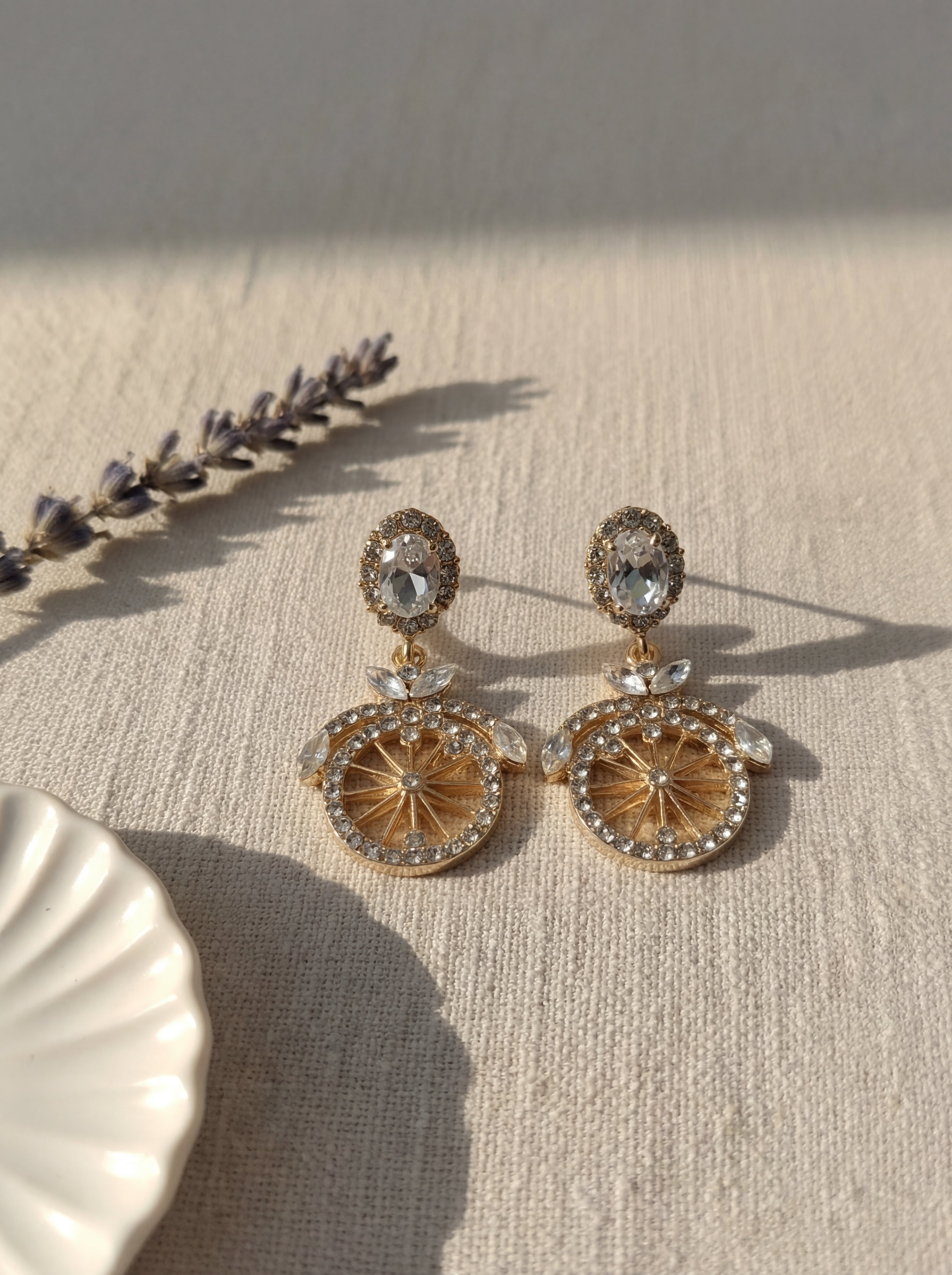 Pair of gold and crystal earrings on a textured surface with lavender.