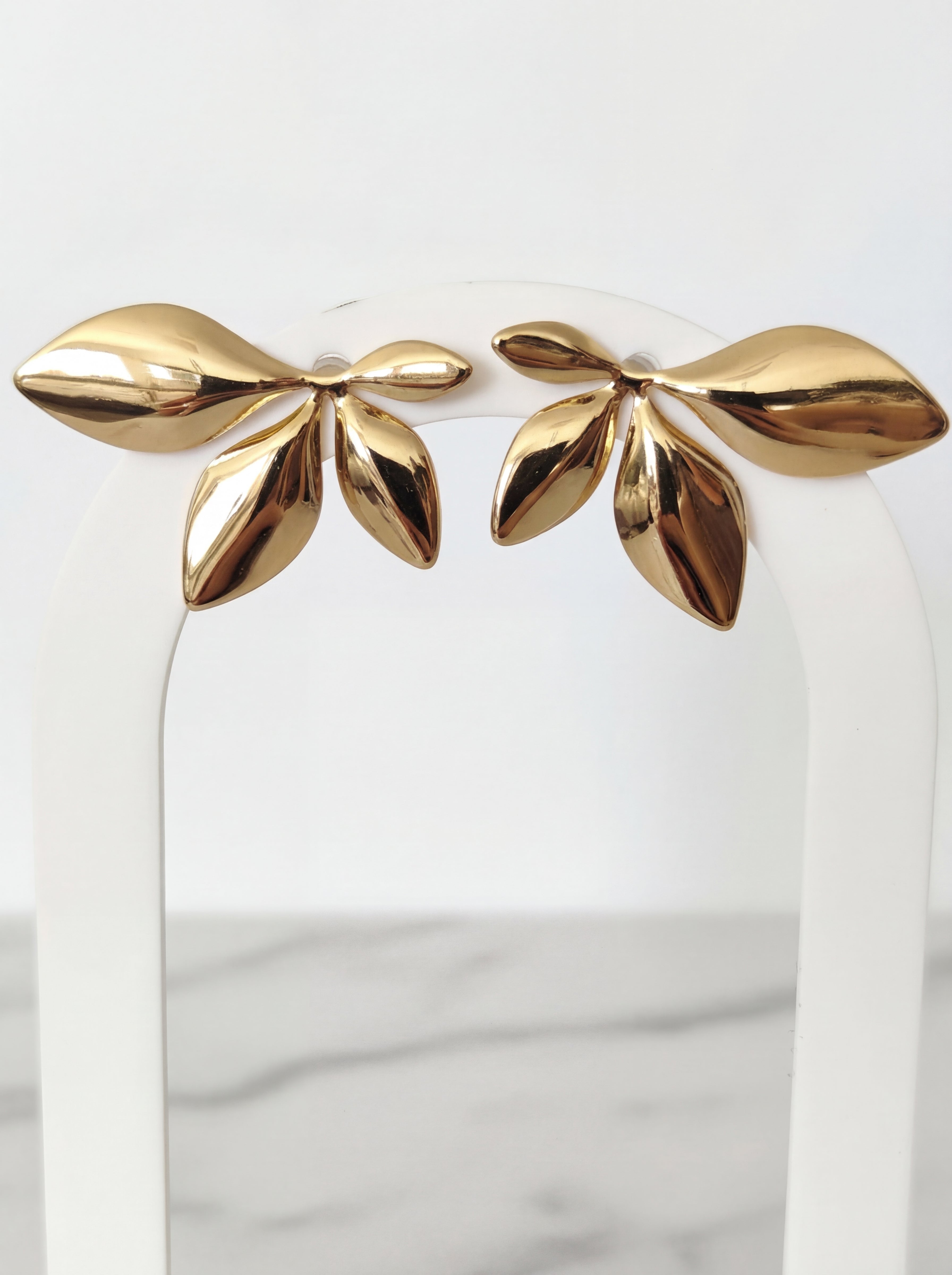 Gold leaf-shaped earrings on a white stand with a marble background