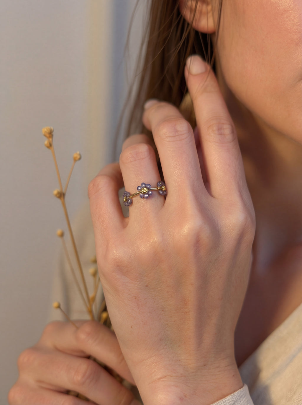 Close-up of a hand wearing a ring with a floral design, holding a small plant.