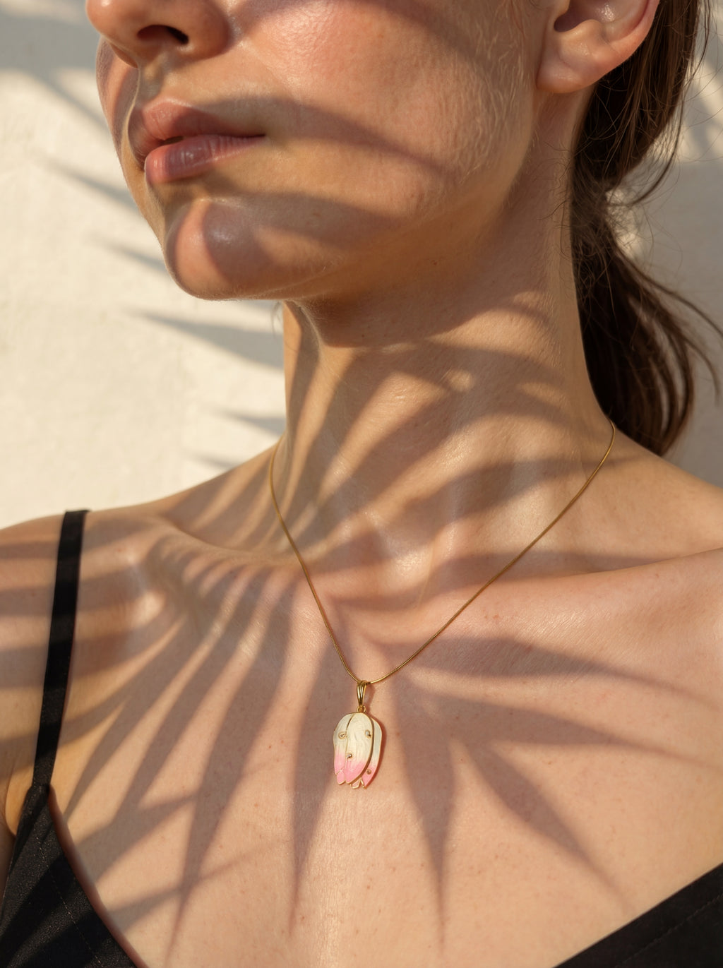 Close-up of a person wearing a necklace with a pendant, set against a neutral background.