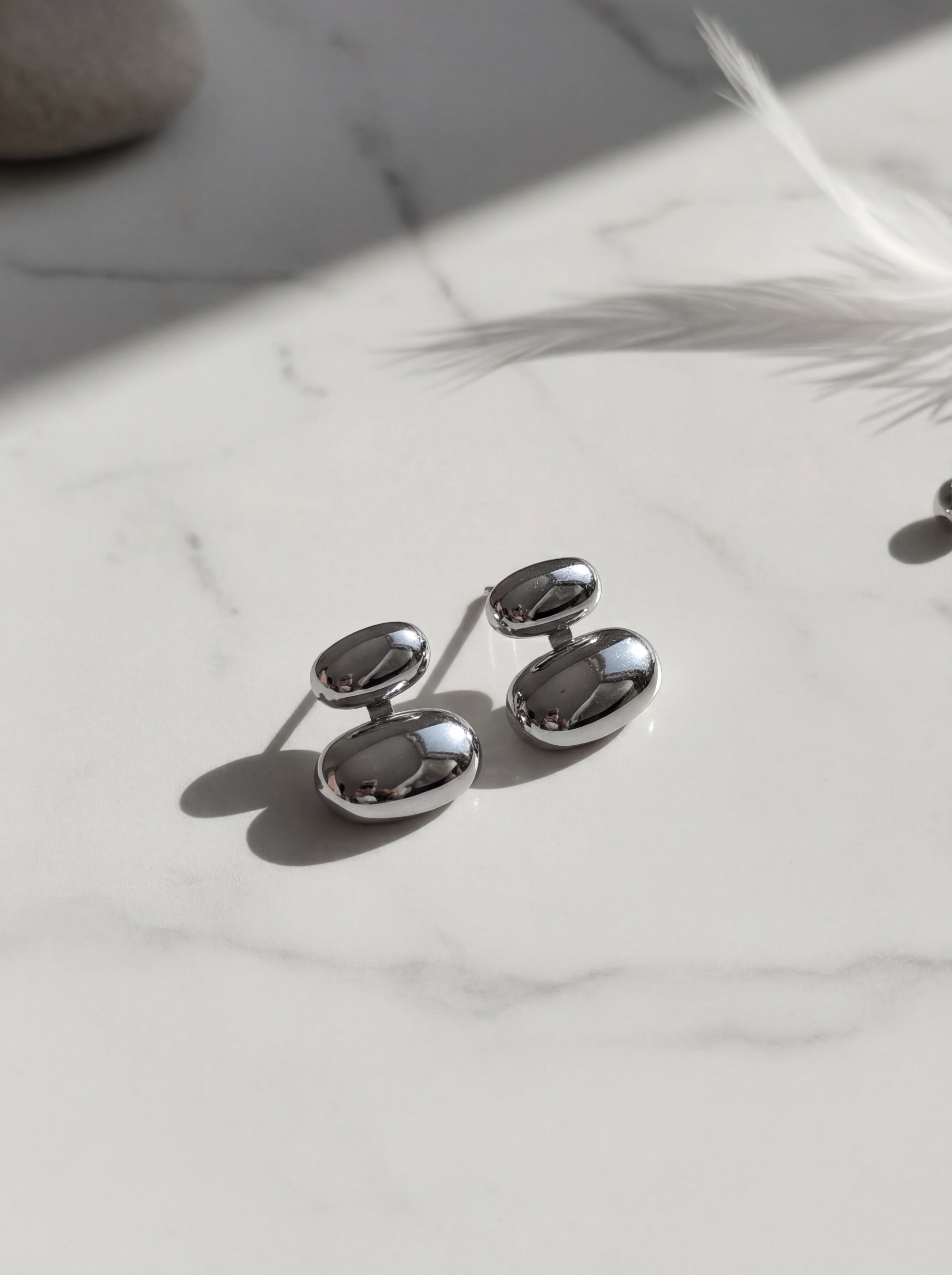 Silver oval-shaped earrings on a marble surface with a light background
