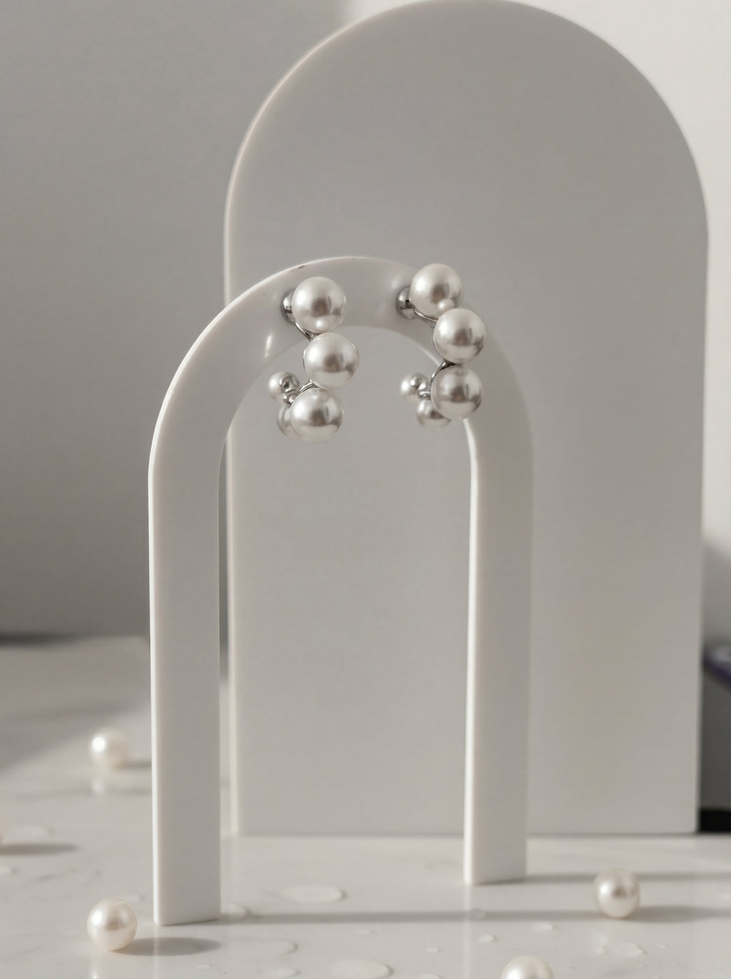 Pearl earrings on a white arch stand with a neutral background