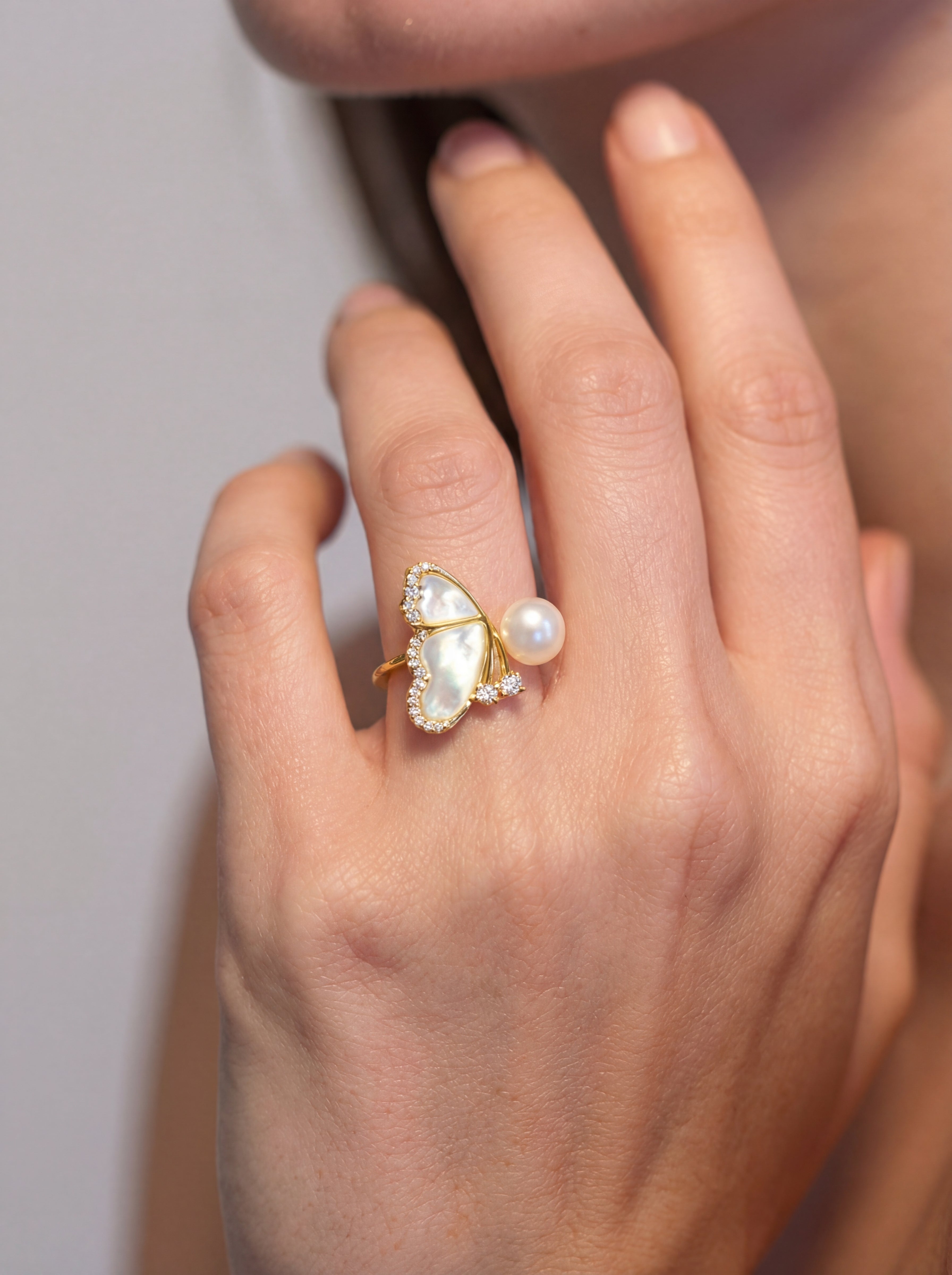 Hand wearing a gold ring with a heart-shaped pearl on a neutral background