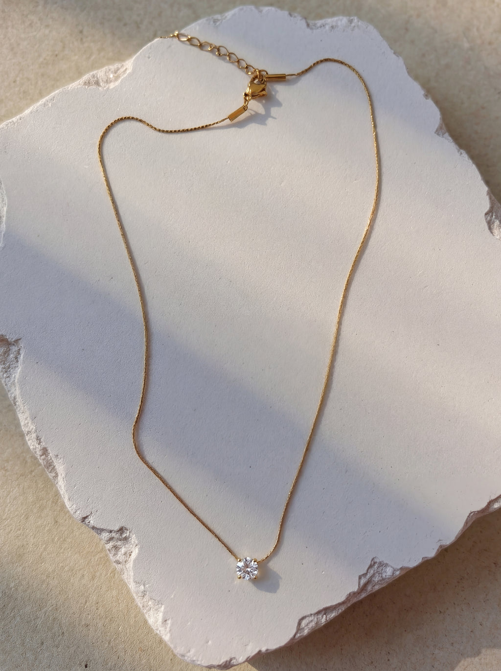 Gold necklace with a diamond pendant on a white stone surface
