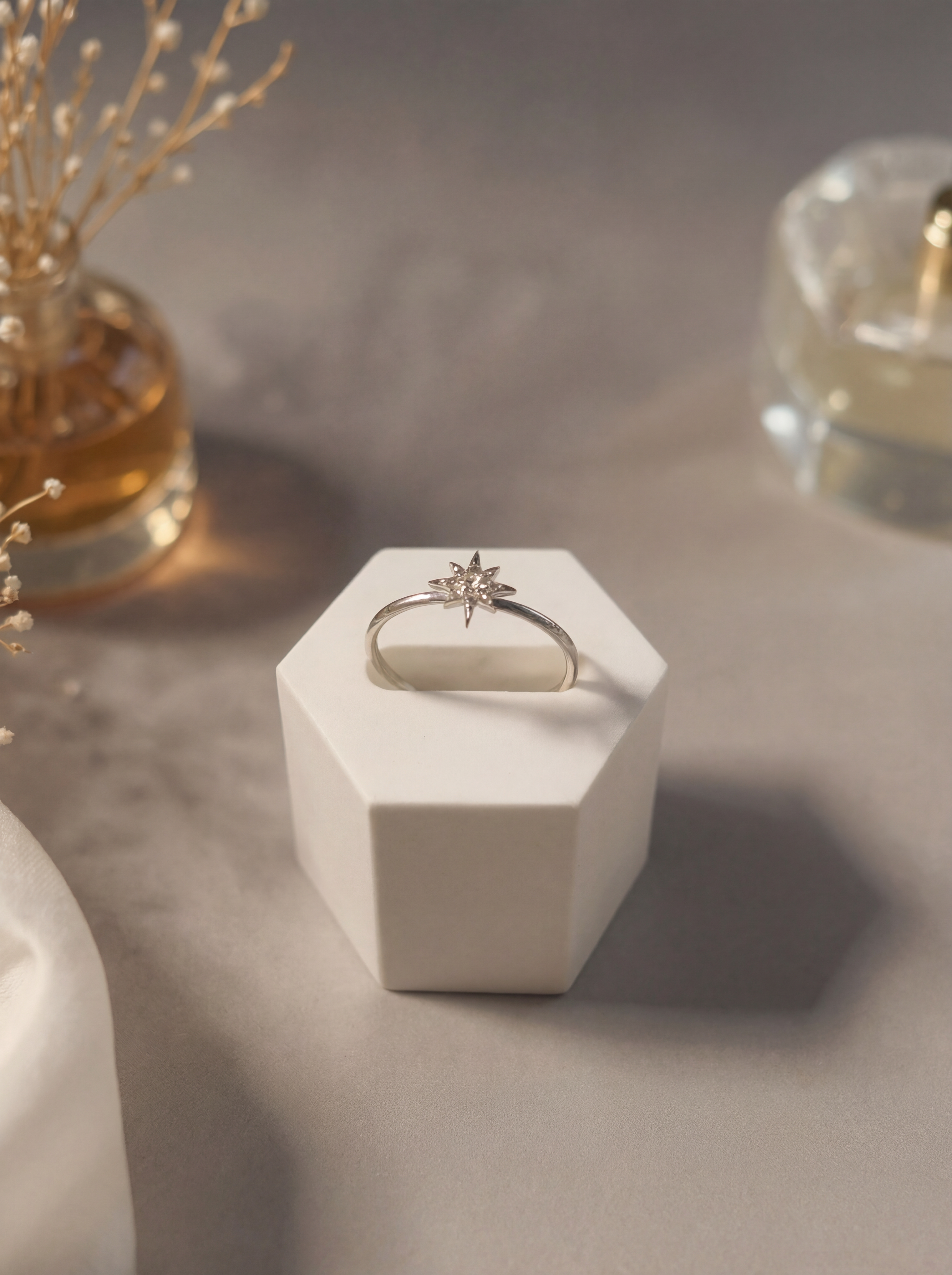 Gold ring with a star design on a white hexagonal stand, surrounded by decorative elements.