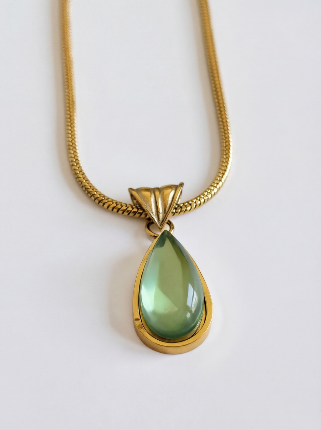 Gold necklace with a green teardrop pendant on a white background