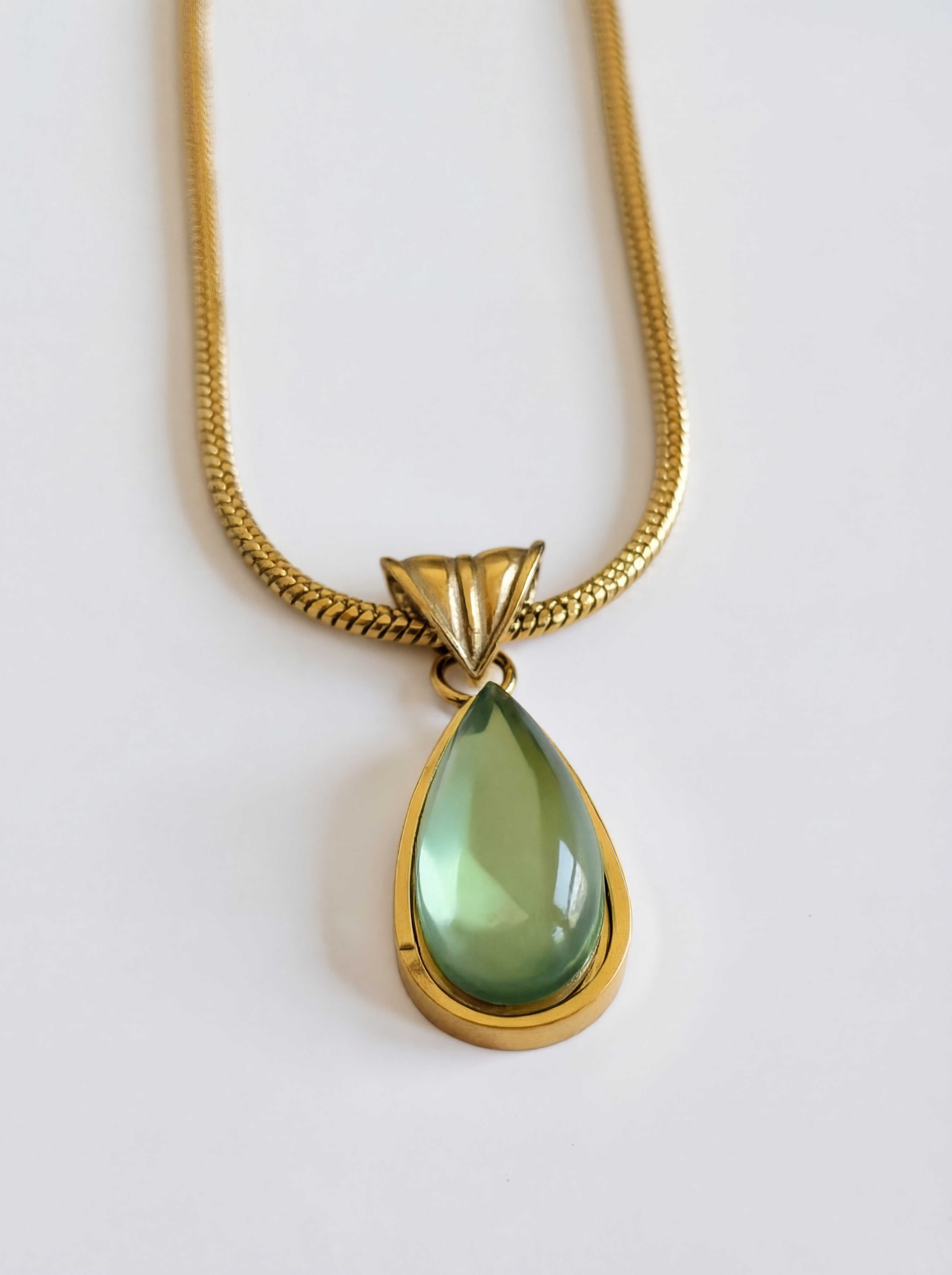 Gold necklace with a green teardrop pendant on a white background