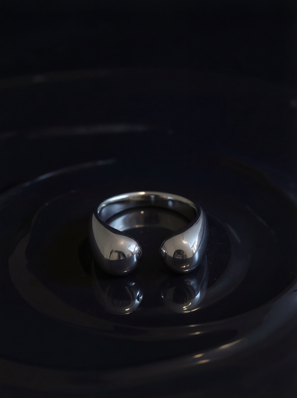 Silver ring on a reflective black surface with a dark background