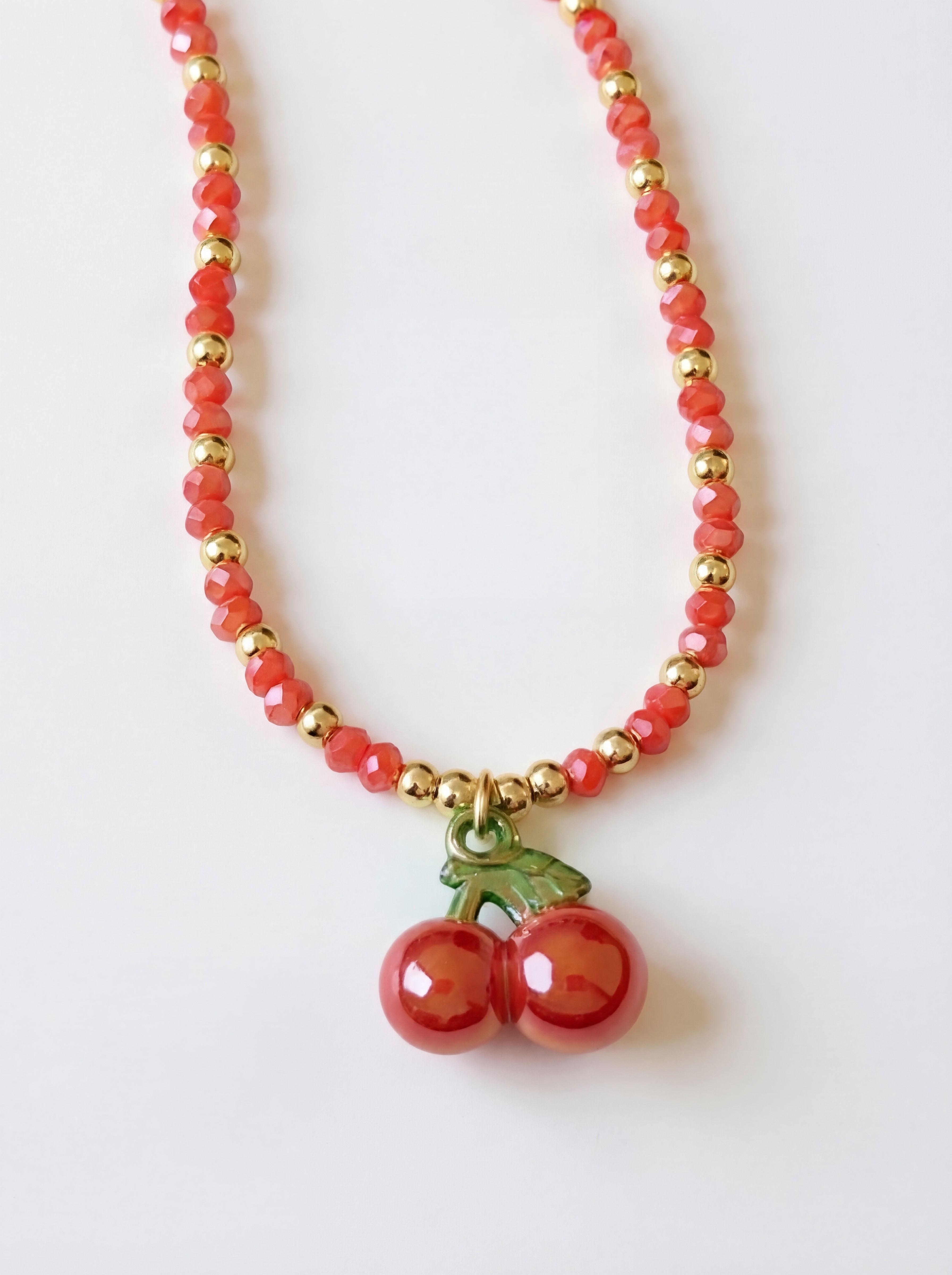 Necklace with red beads and cherry charm on a white background