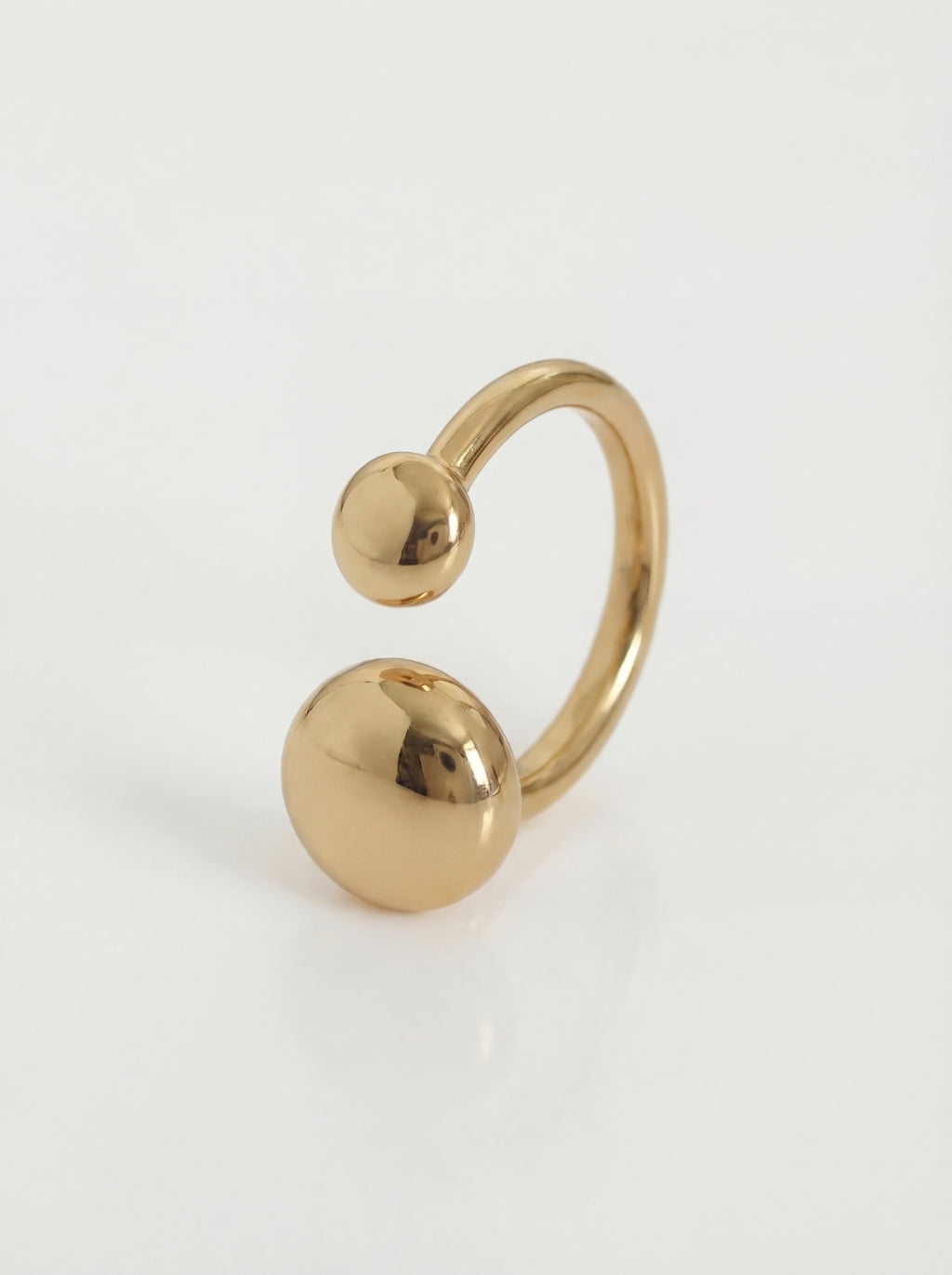 Gold ring with two spherical ends on a light gray background