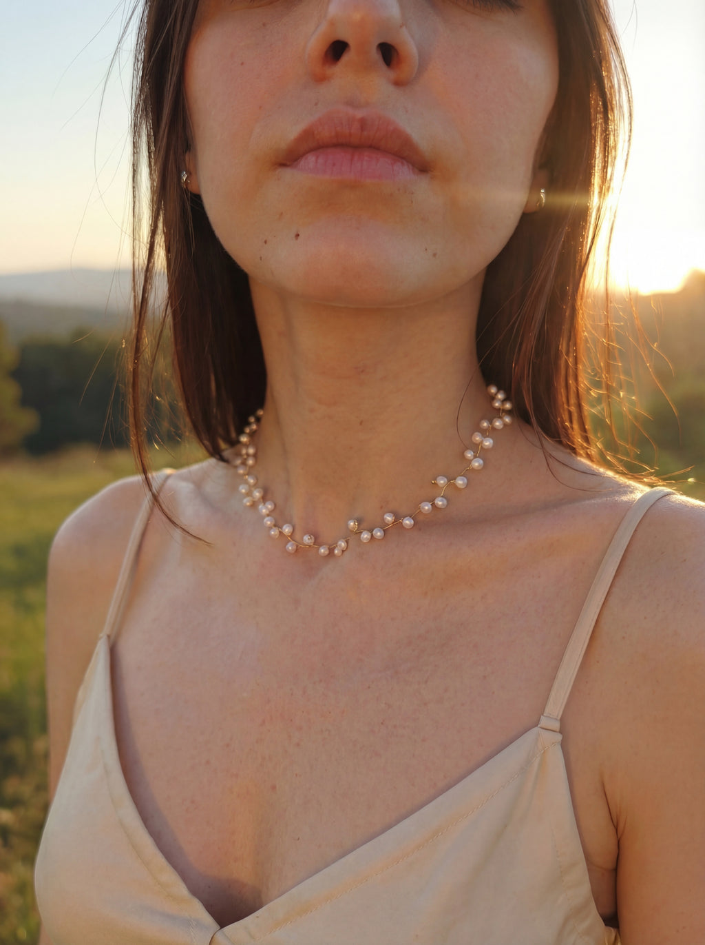 Woman wearing a pearl necklace in a natural setting with sunlight