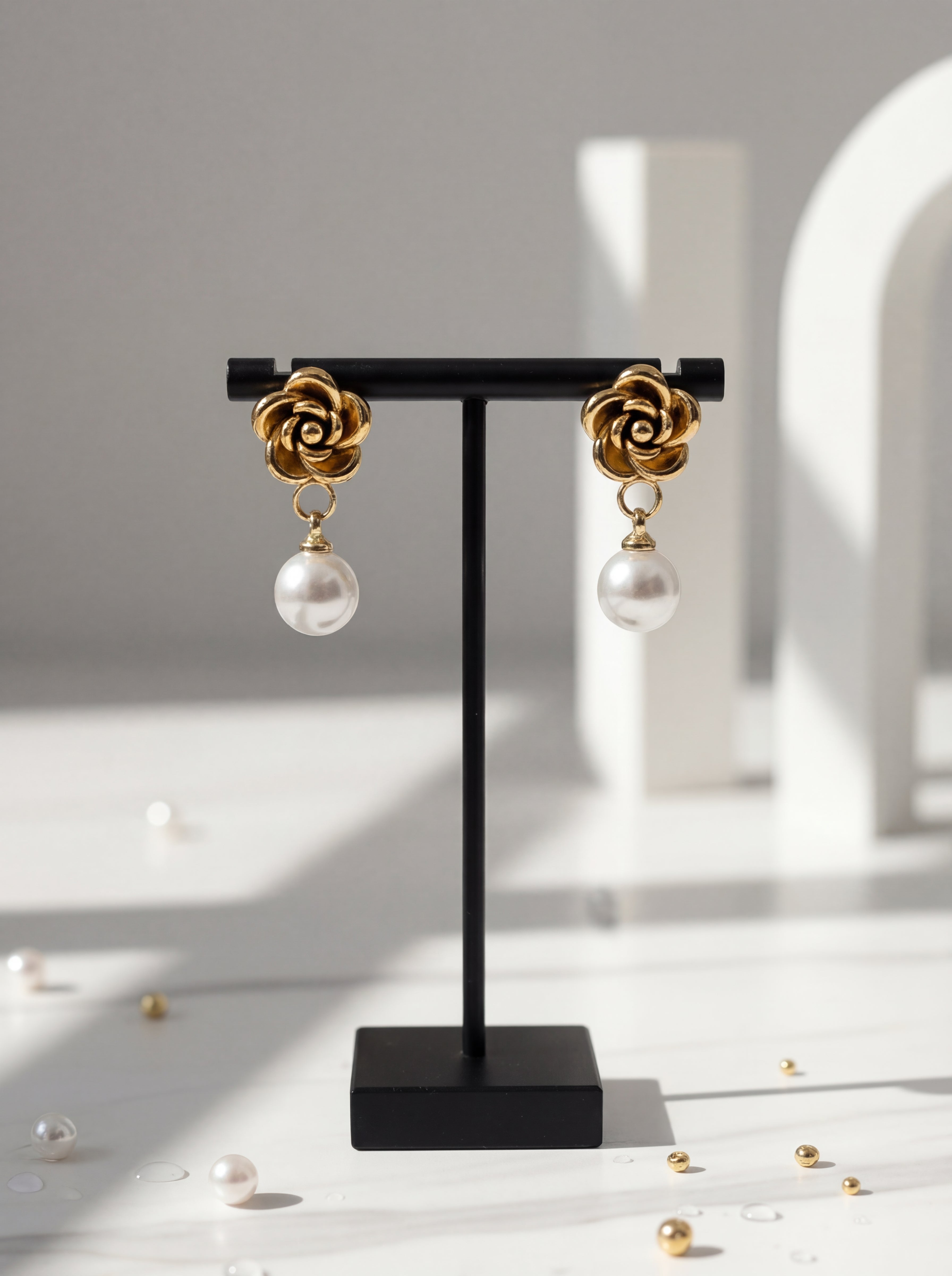 Gold and pearl earrings on a black stand with scattered pearls on a light surface.