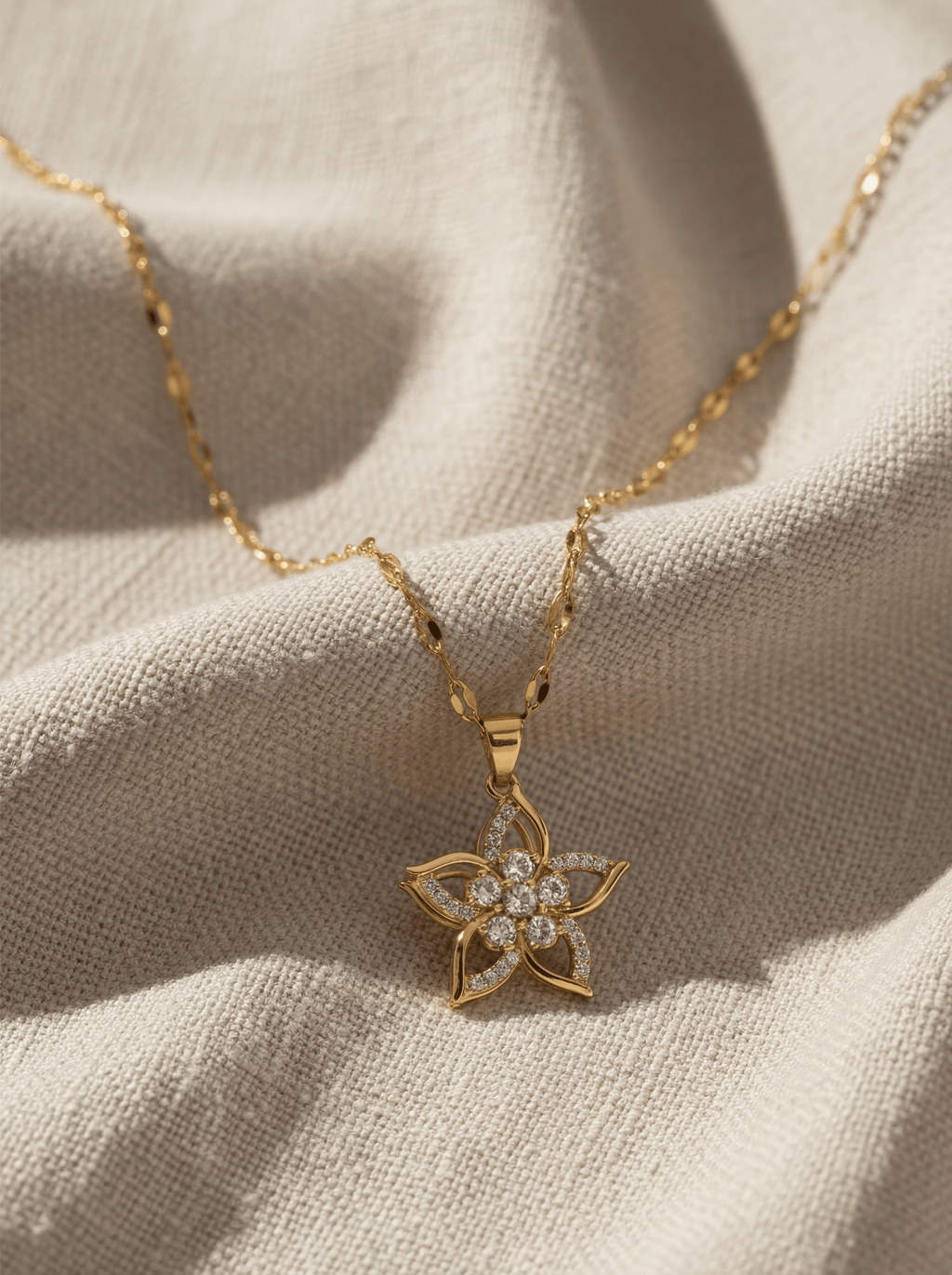 Gold necklace with a star-shaped pendant on a beige fabric background