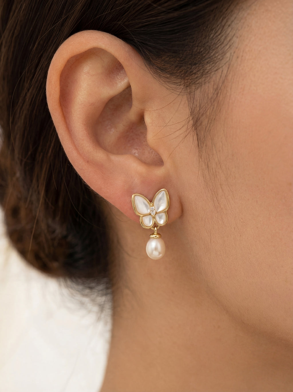 Butterfly earring with pearl drop worn by a person