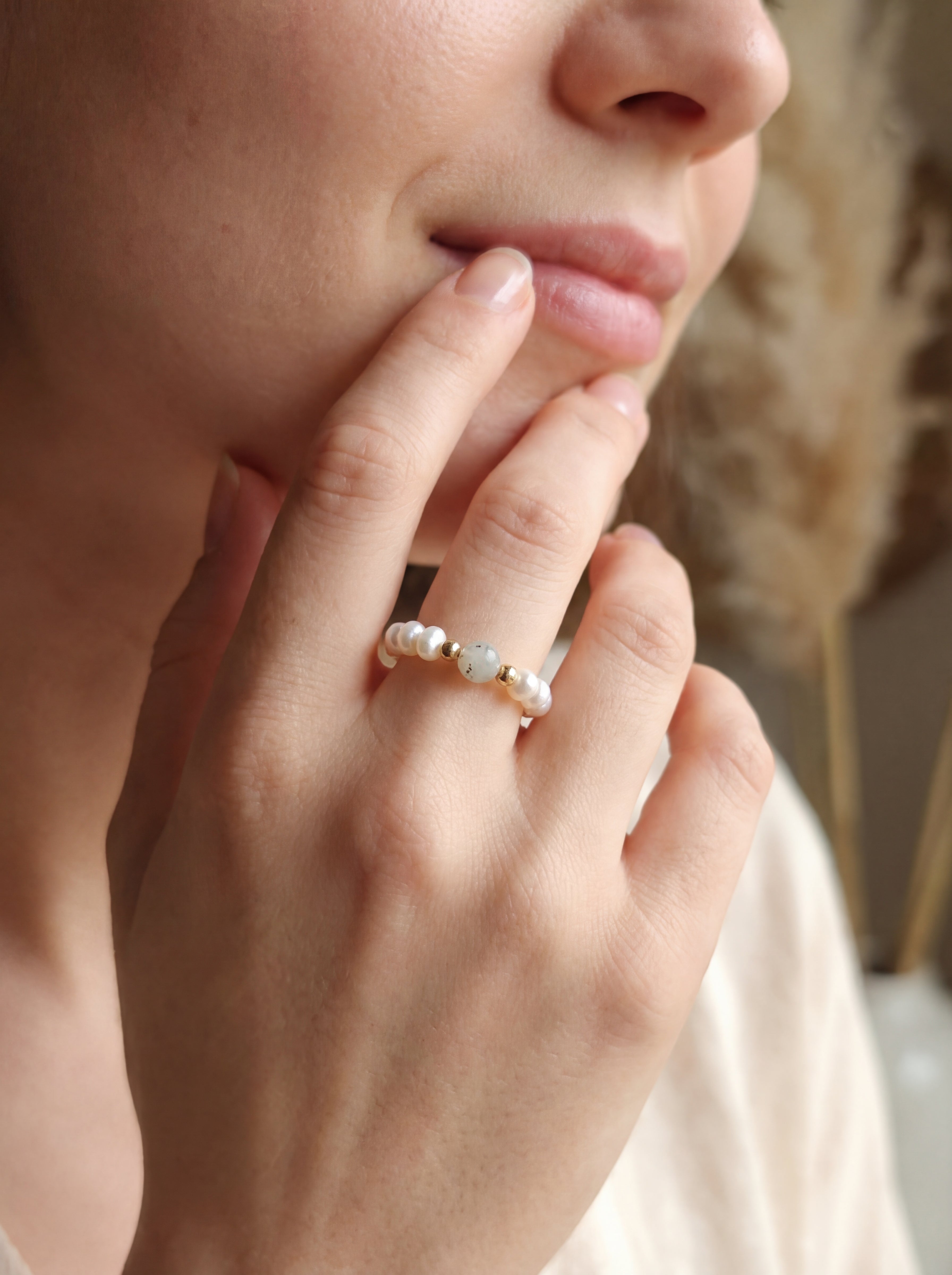 Close-up of a hand wearing a pearl ring with a blurred background