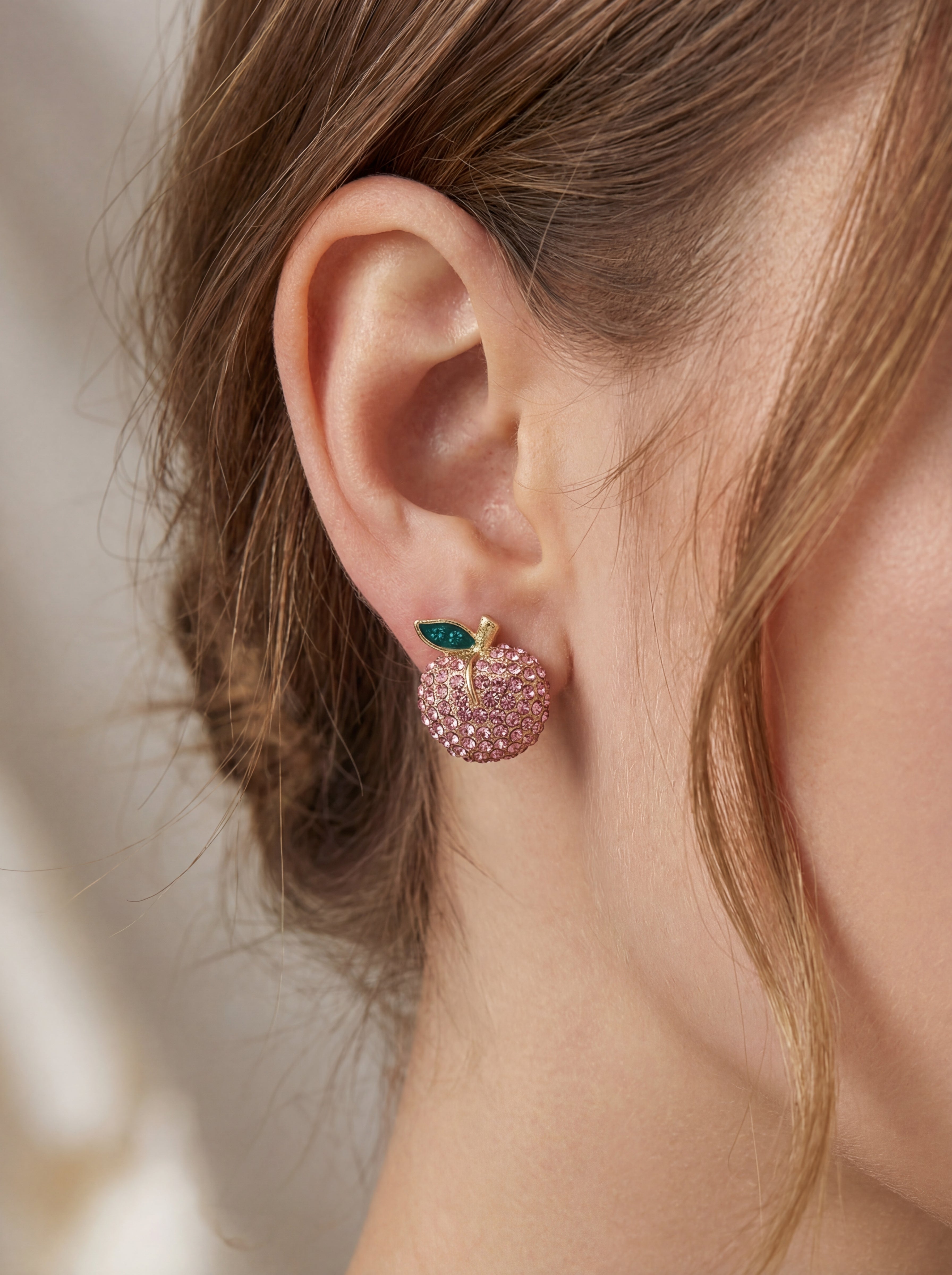 Close-up of a person wearing pink apple-shaped earrings with green gemstones.