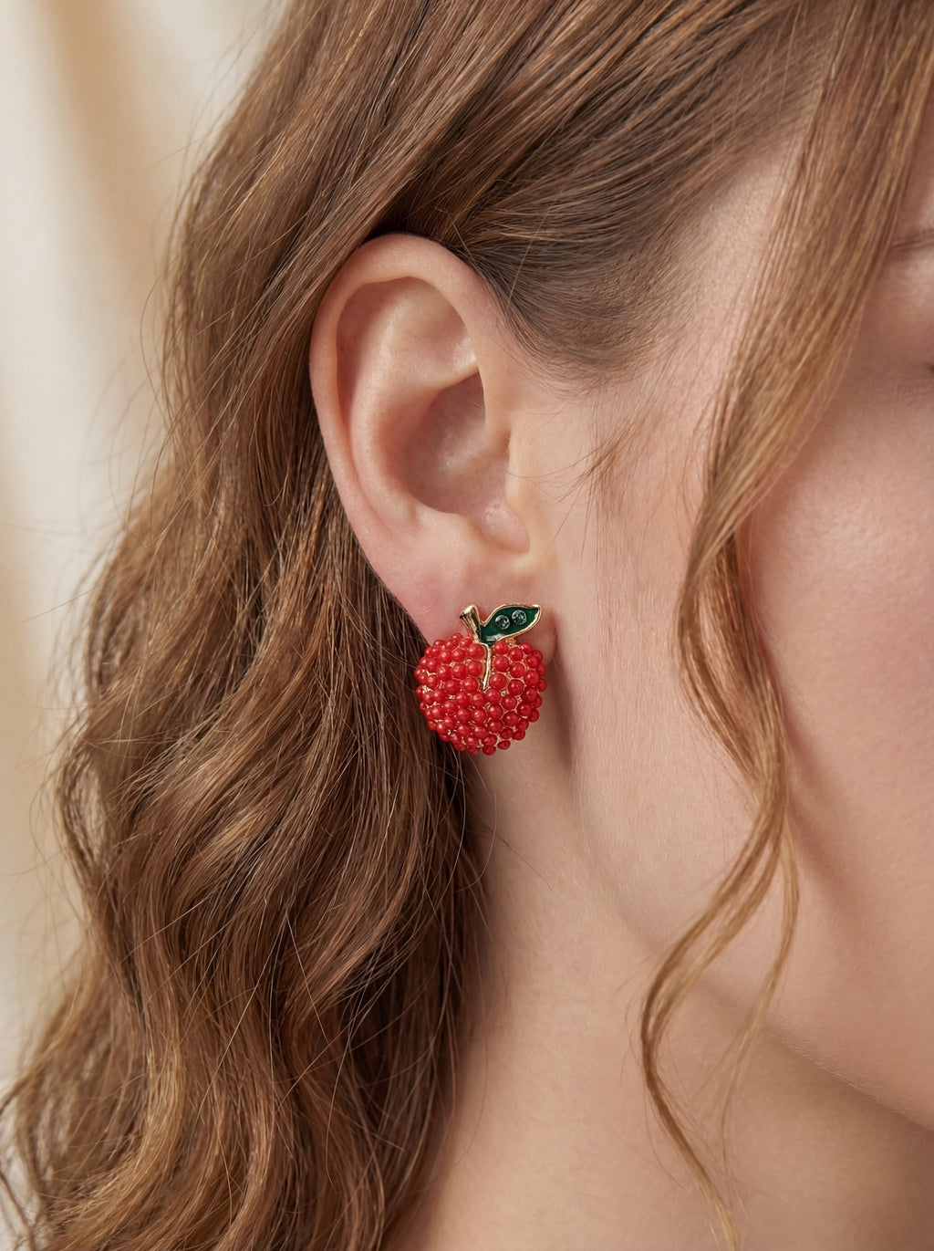 Close-up of a person wearing red berry-shaped earrings with green leaves.