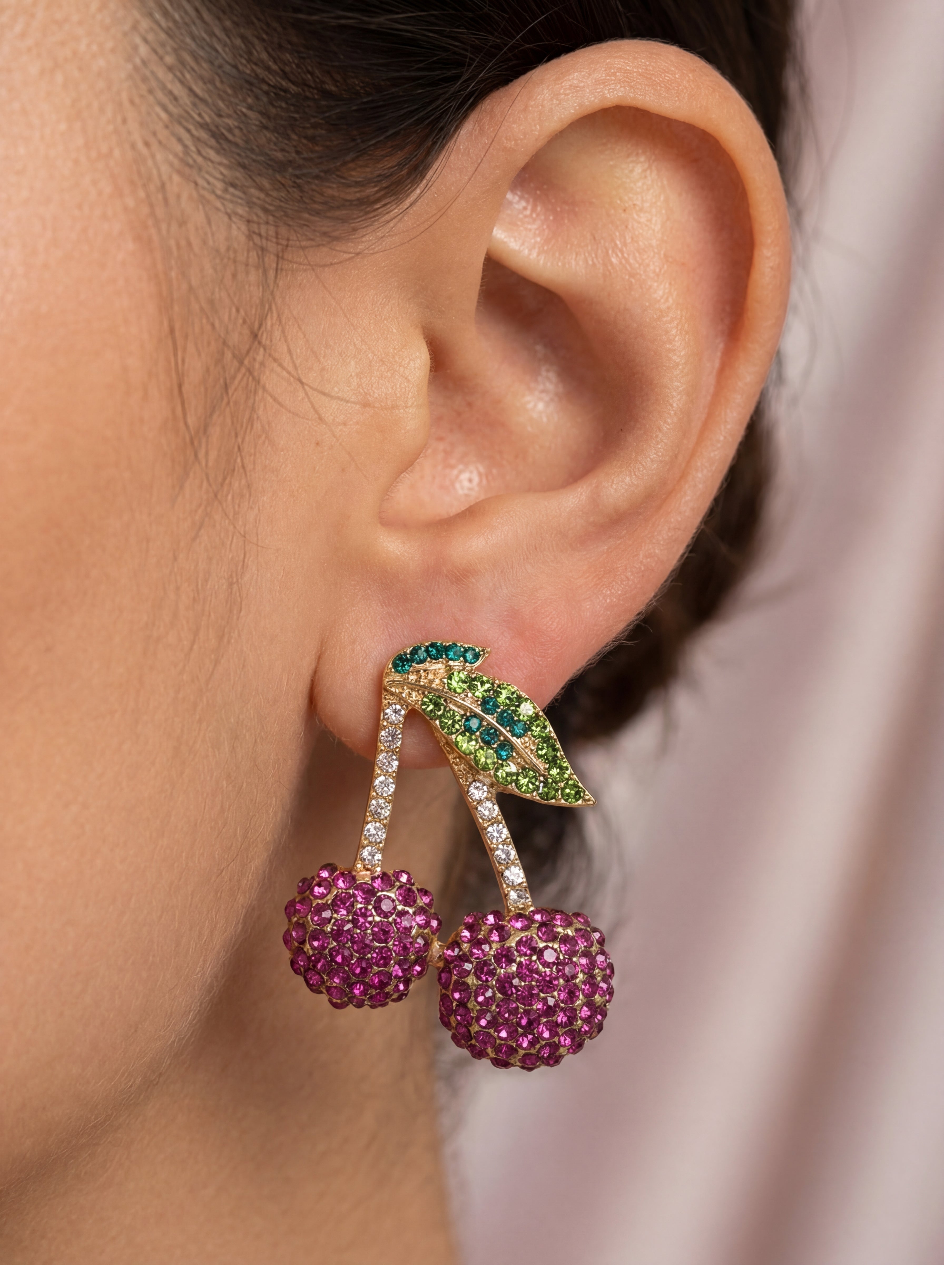 Close-up of an ear wearing a decorative earring with pink and green elements.