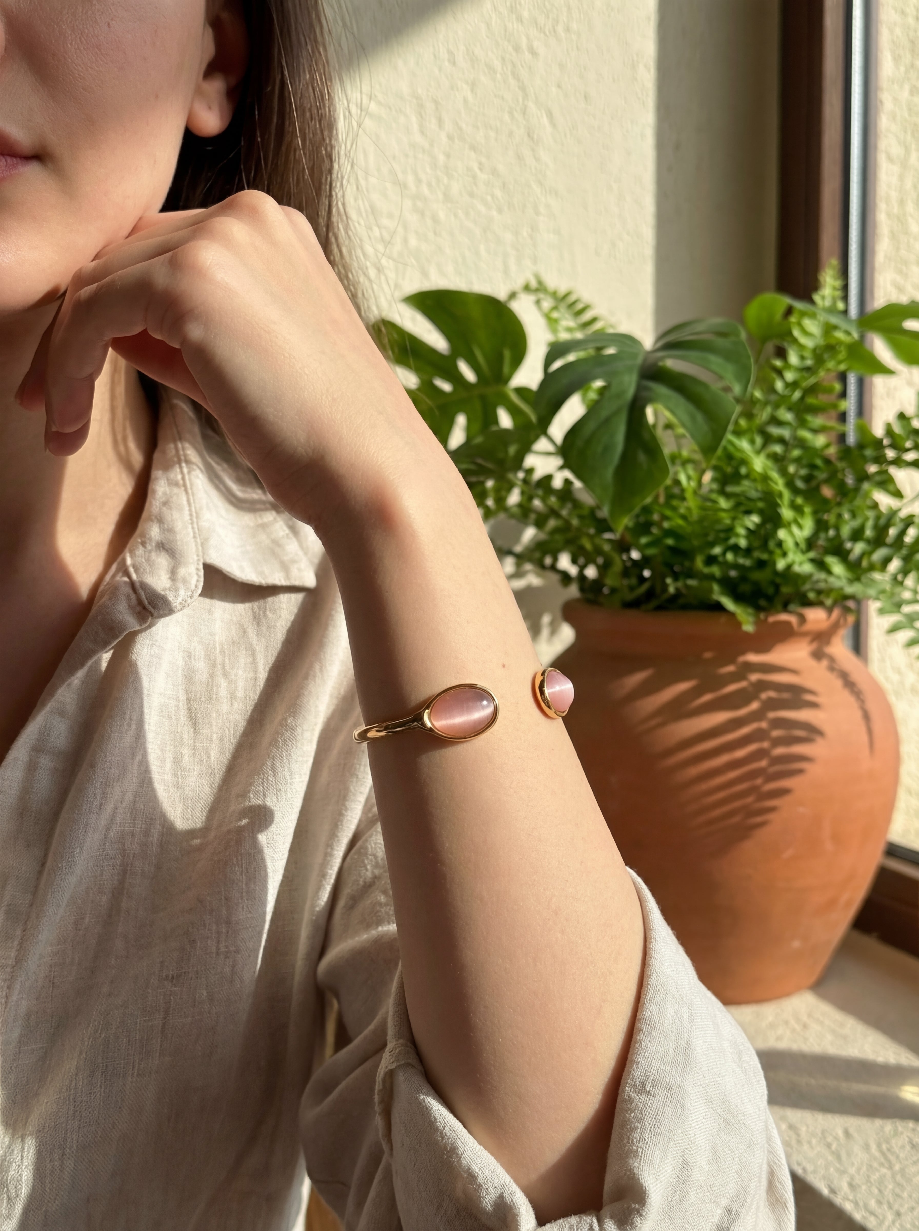 Person wearing a bracelet with pink stones, sitting by a window with a plant in the background