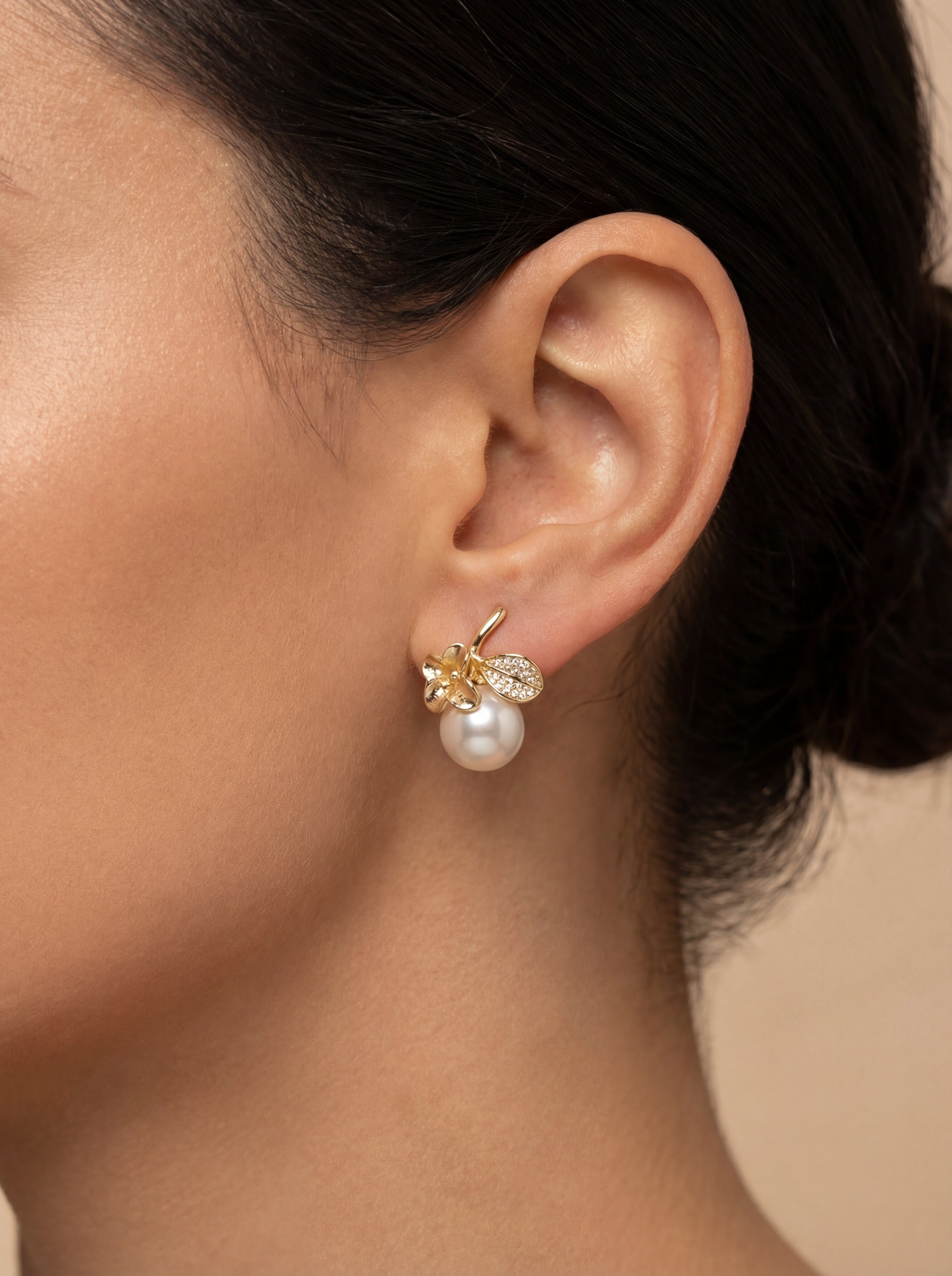 Close-up of an ear wearing a pearl earring with gold and diamond accents.
