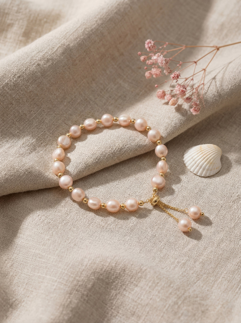 Pearl bracelet on a beige fabric background with dried flowers and a shell.