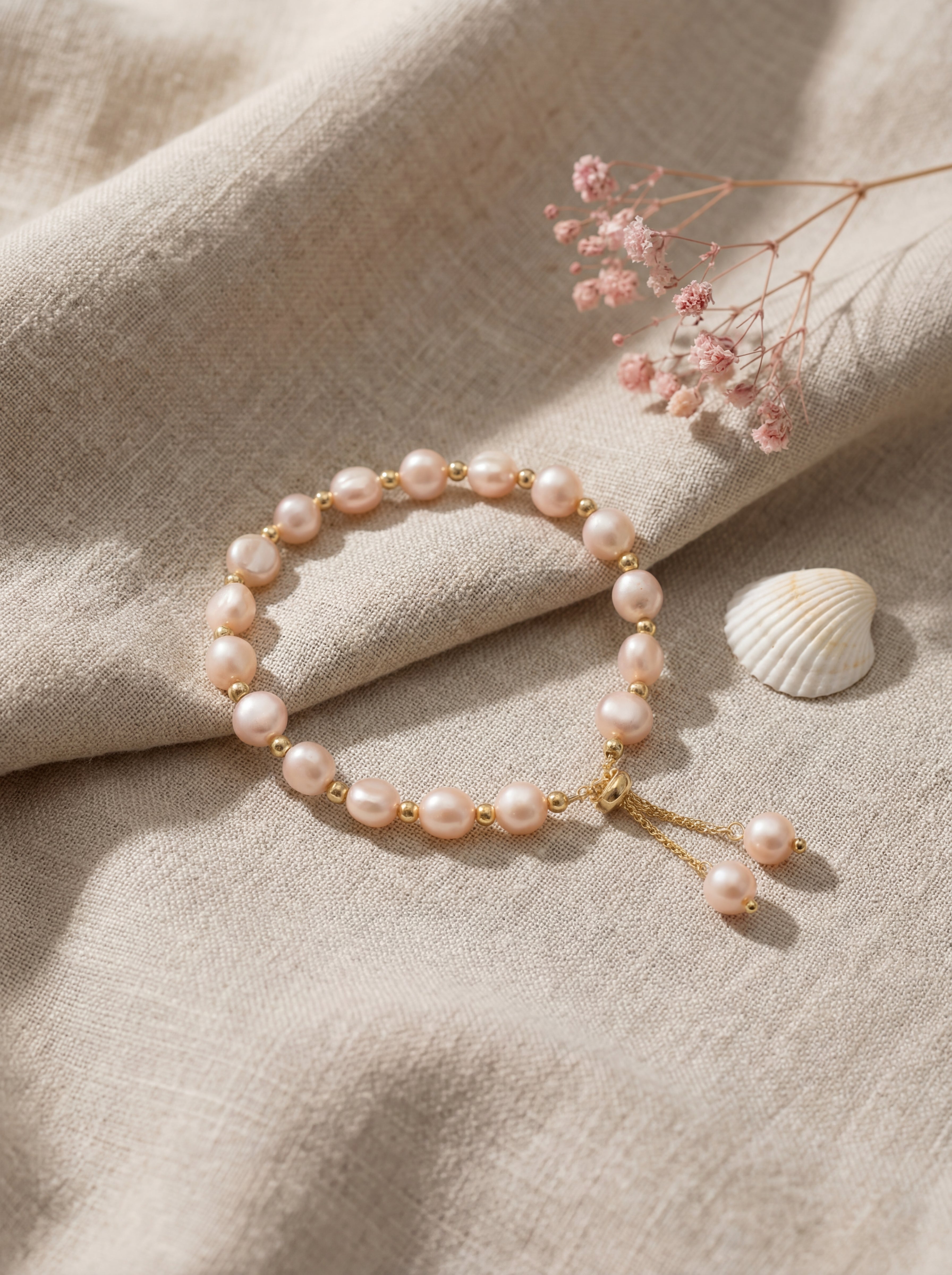 Pearl bracelet on a beige fabric background with dried flowers and a shell.