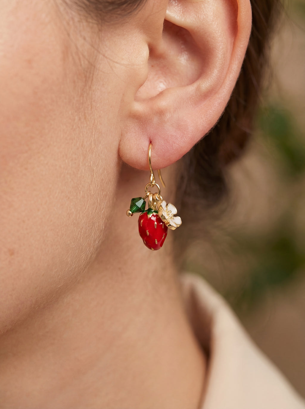 Close-up of an ear wearing a red and green earring with gold accents.