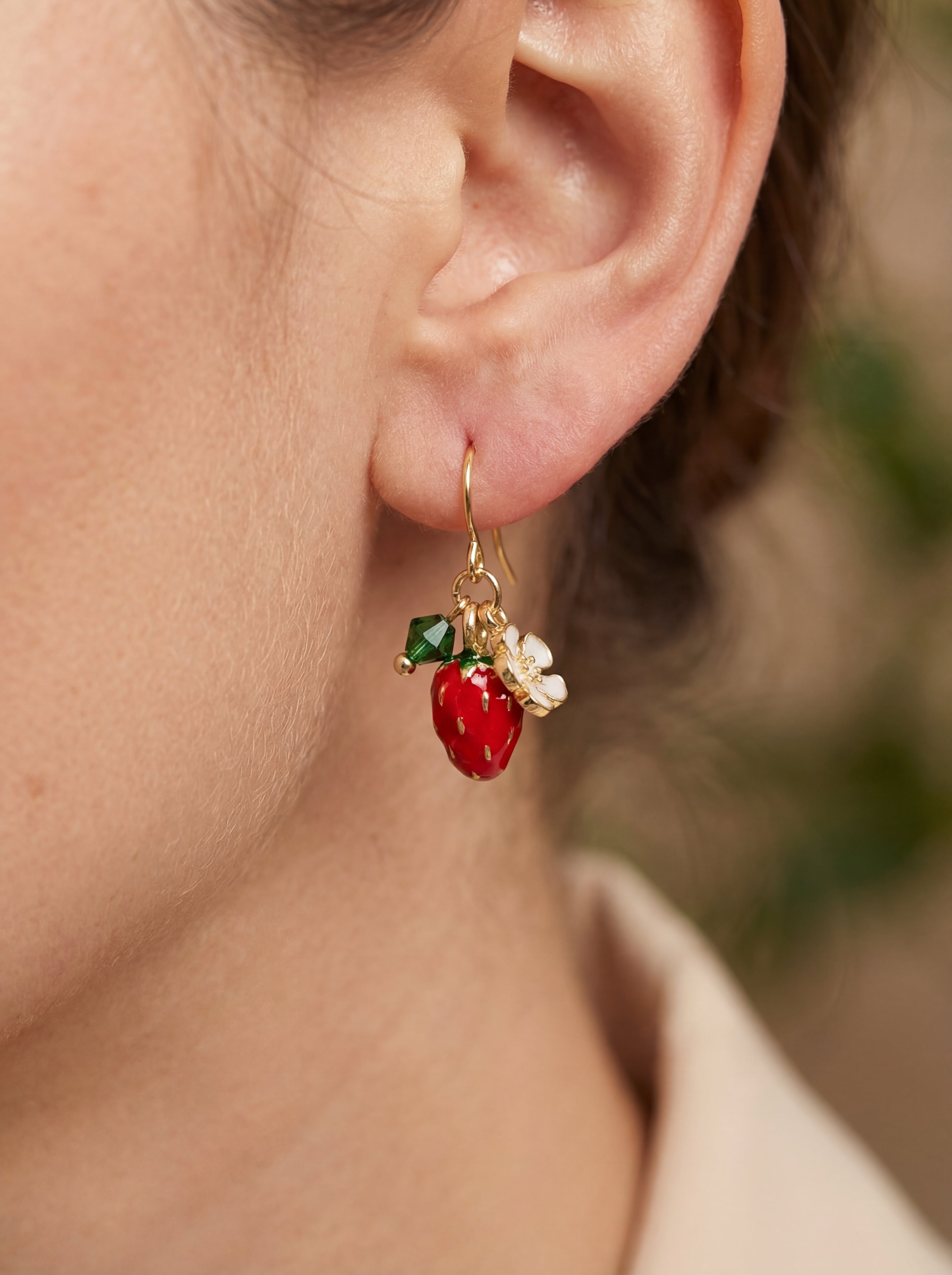 Close-up of an ear wearing a red and green earring with gold accents.