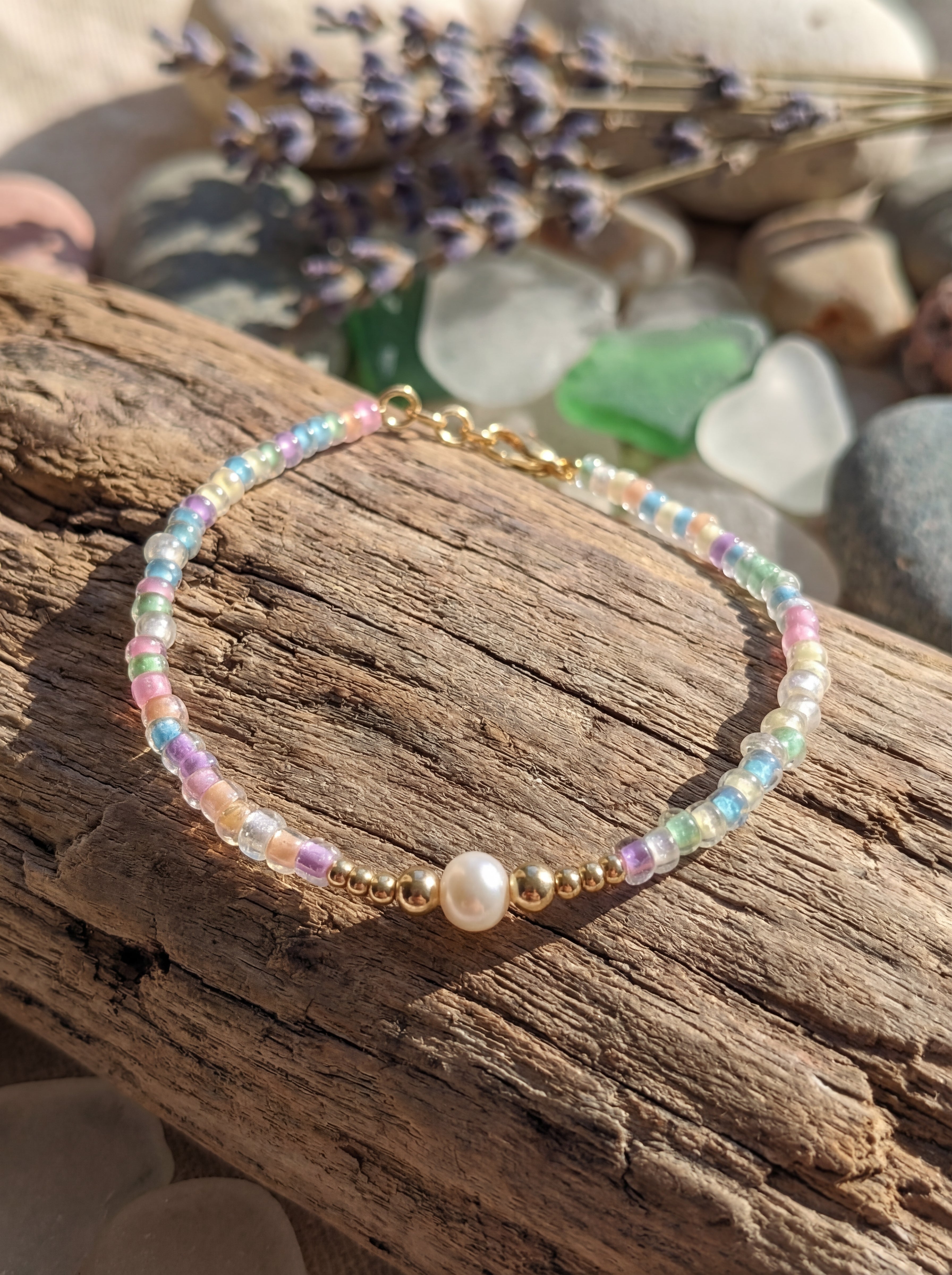 Multicolored beaded bracelet with a pearl on a wooden surface with pebbles in the background